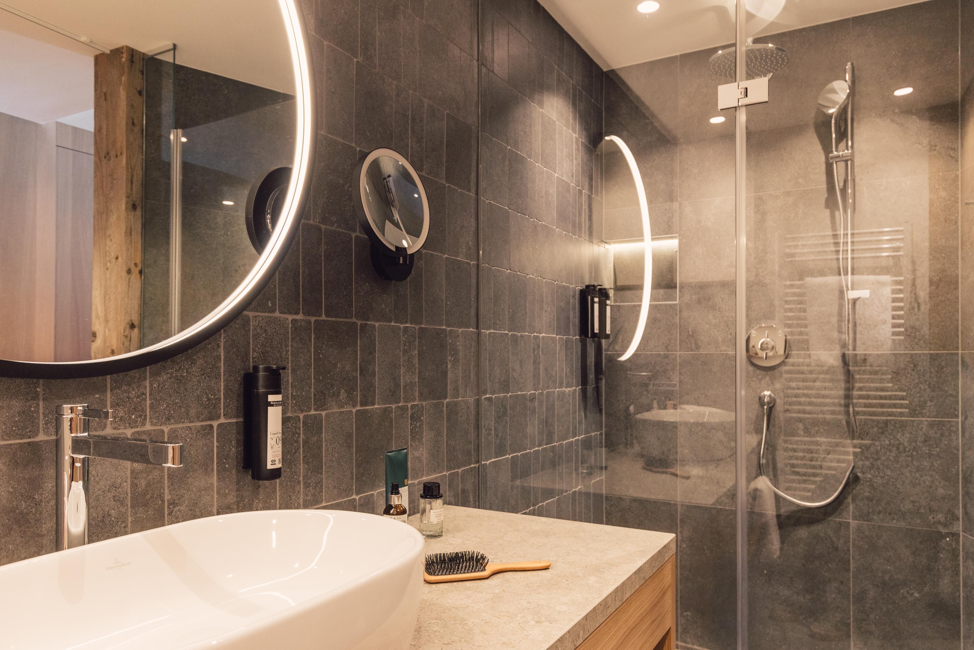 Ein modernes Badezimmer mit einem eleganten Design. Die Dusche ist mit Glasabtrennungen versehen, und der runde Spiegel sorgt für ein stilvolles Ambiente.