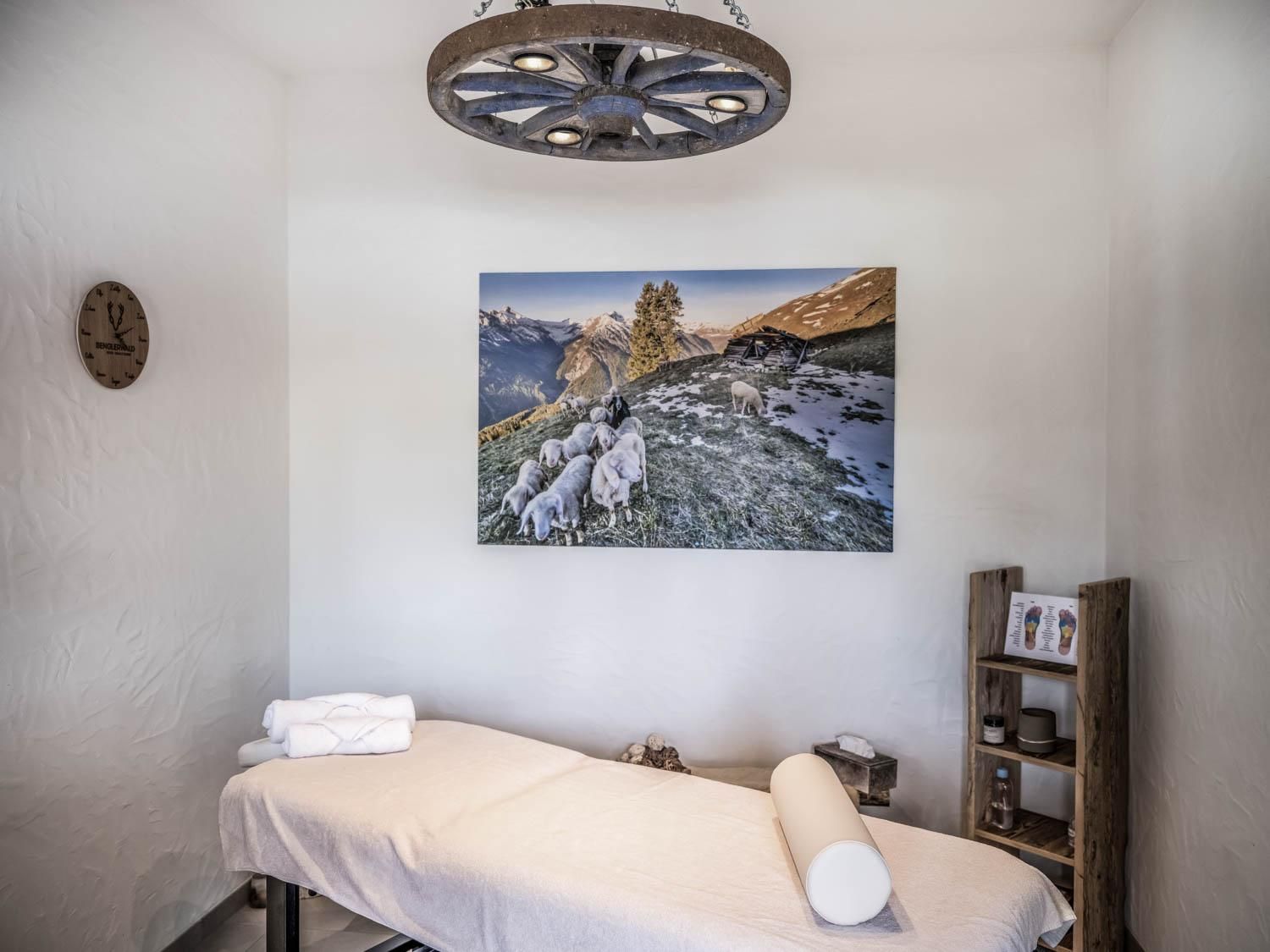 Ein ruhiger Massageraum mit einem Behandlungstisch und einem großen Landschaftsbild an der Wand. Die Atmosphäre ist entspannt und einladend.