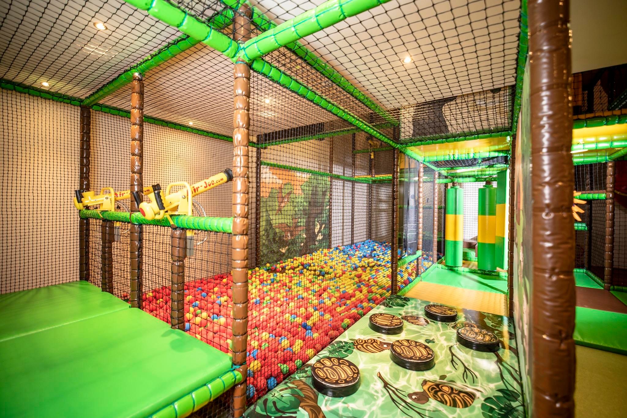 Ein großer Spielbereich mit einem Ballbecken in verschiedenen Farben und grünen Kletterelementen. Der Bereich ist eingezäunt und eignet sich perfekt zum Spielen für Kinder.