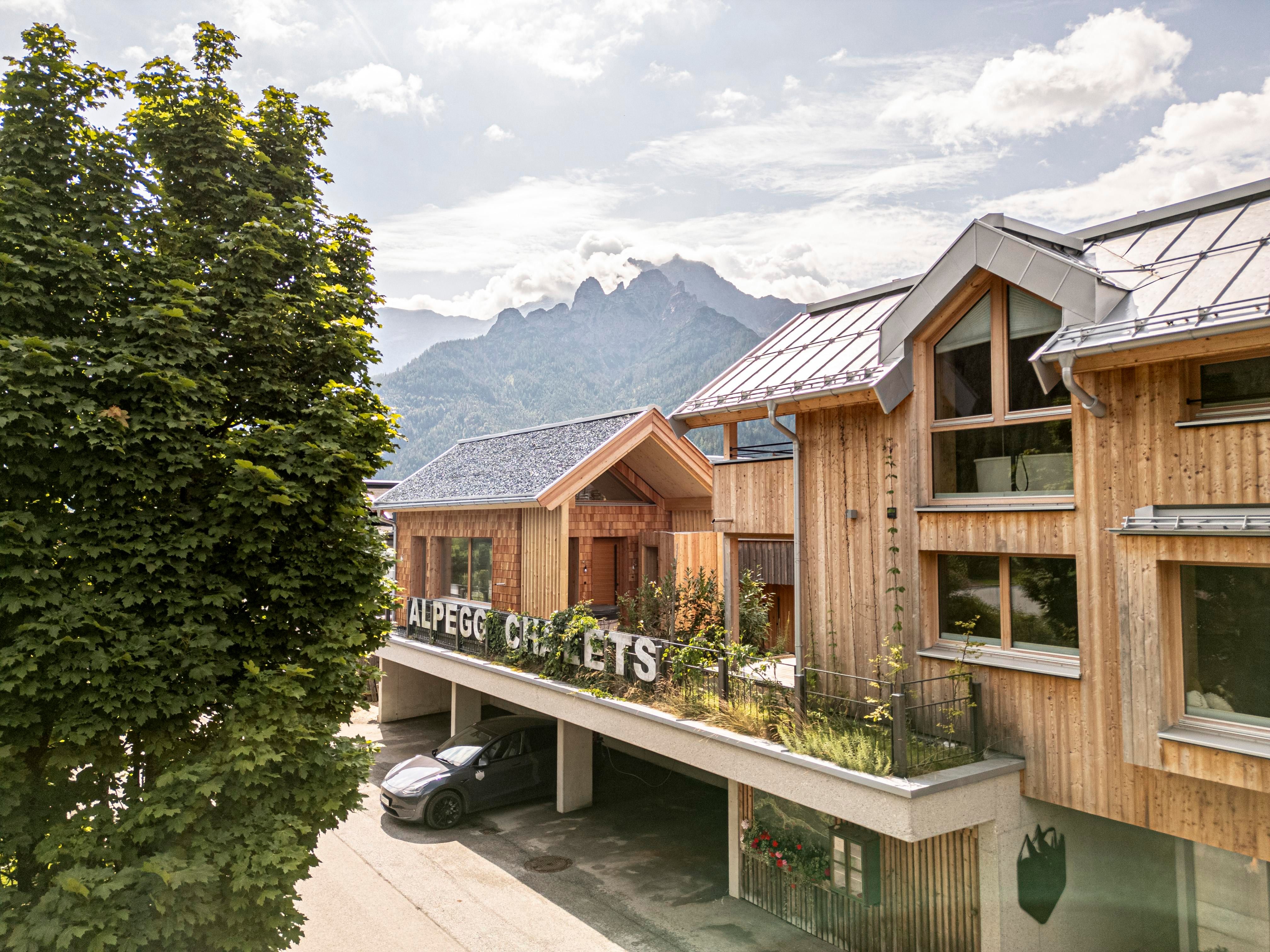 Ein modernes Chaletgebäude aus Holz in den Bergen. Die Umgebung ist grün und einladend, mit einem klaren Himmel im Hintergrund.