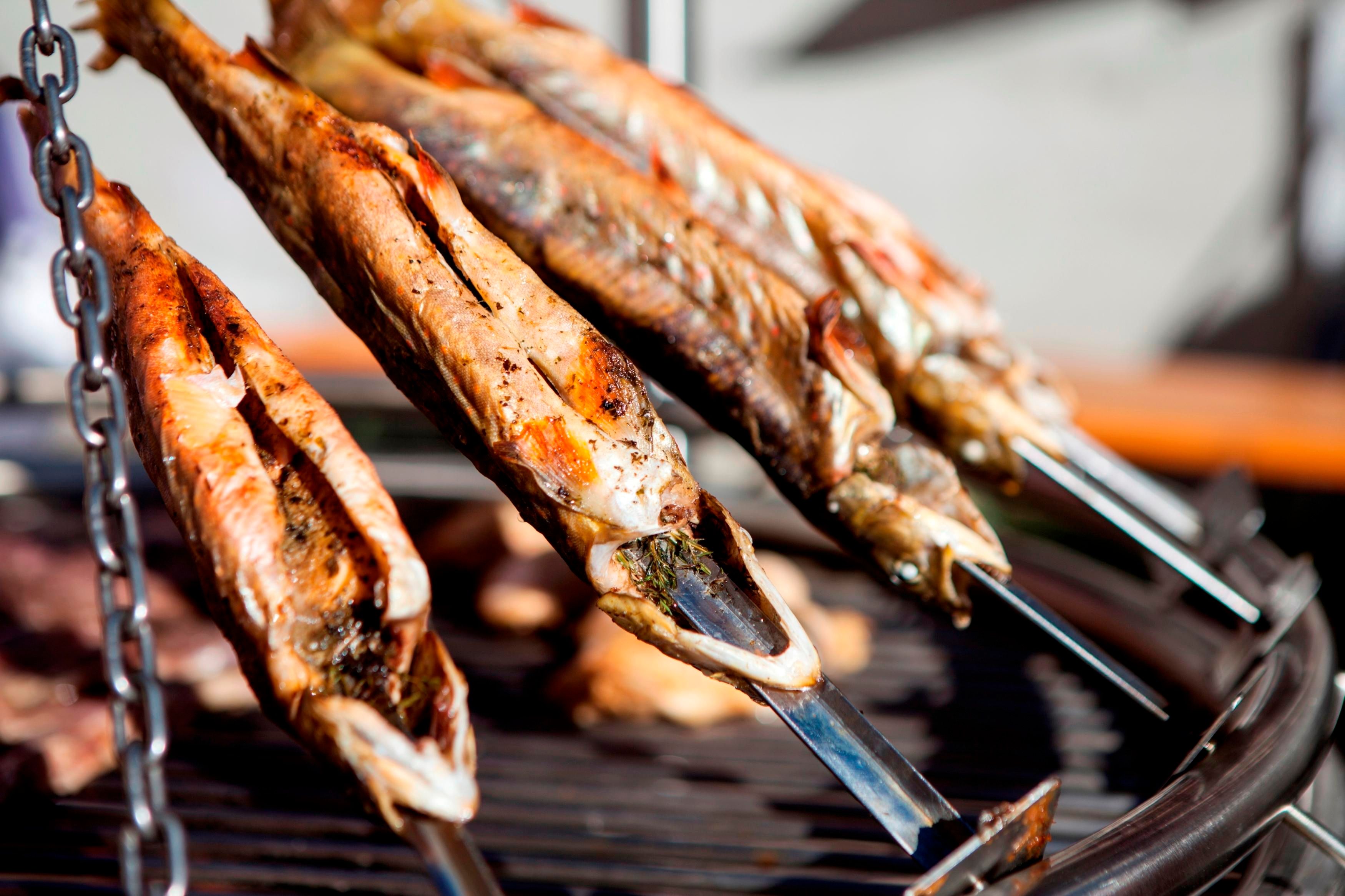 Gegrillte Fische hängen an Spießen über dem Grill. Sie sind goldbraun und sehen köstlich aus.