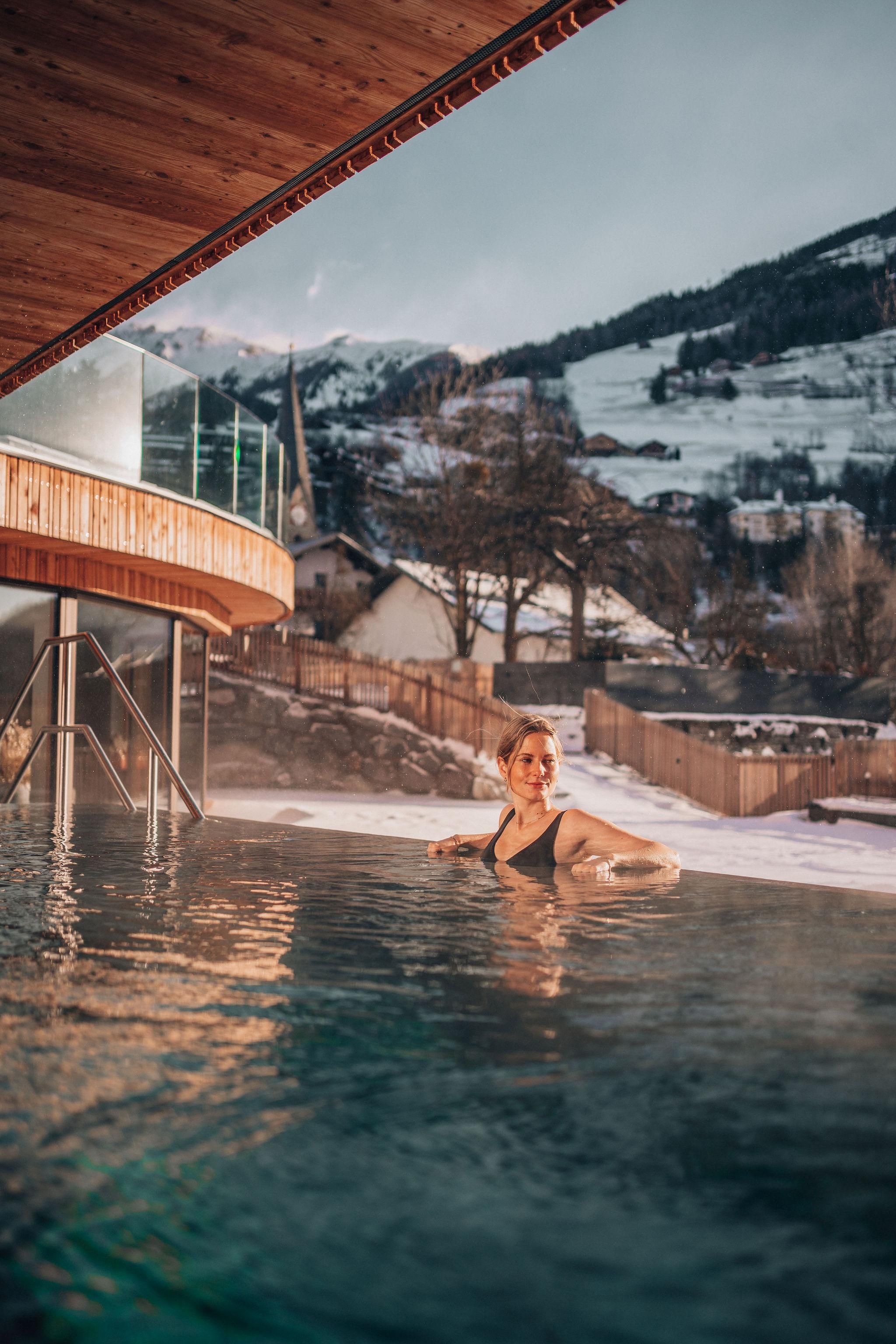 Ein warmer Außenpool mit einem schönen Ausblick auf schneebedeckte Berge. Eine Frau genießt das warme Wasser in der natürlichen Umgebung.