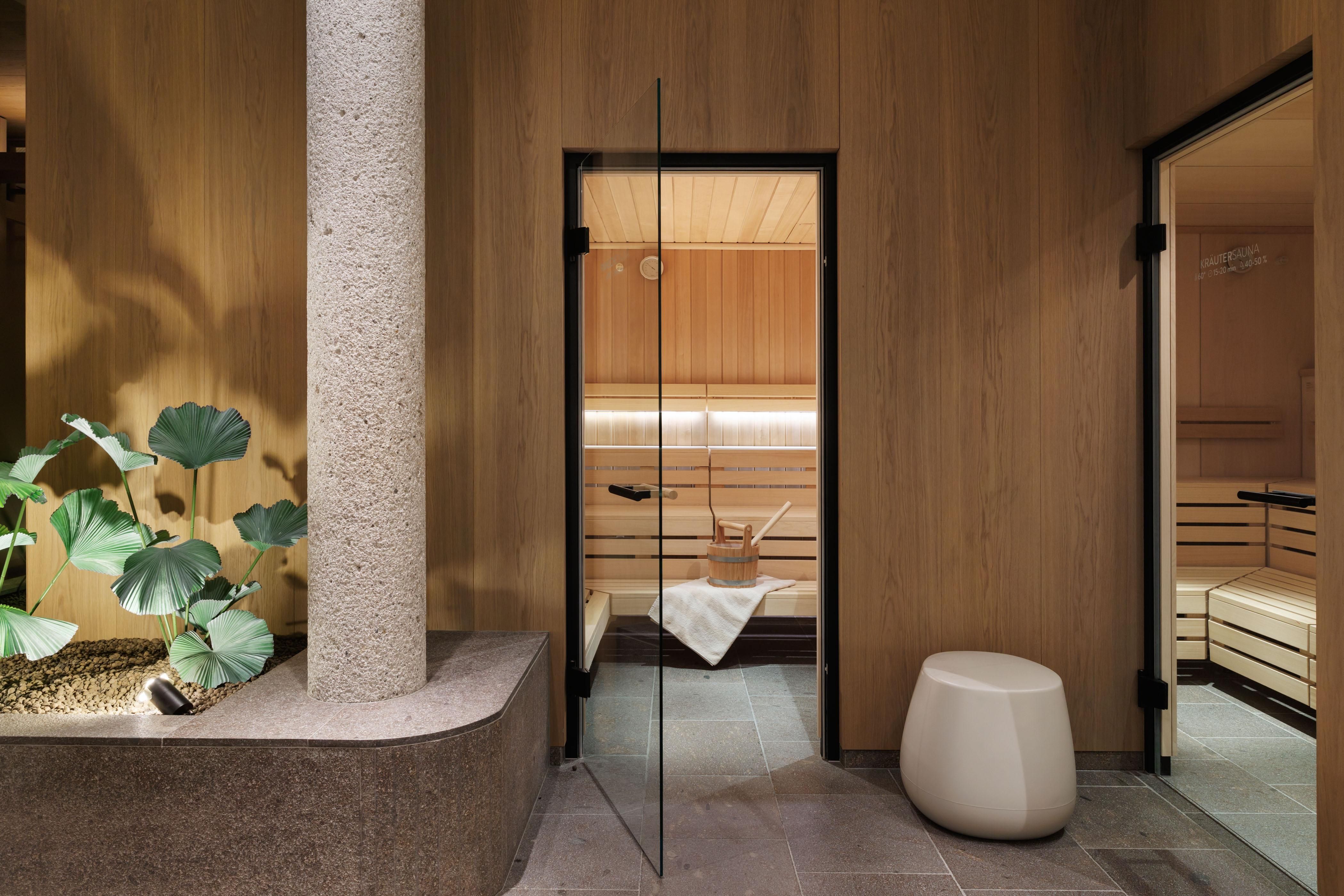 Ein moderner Wellnessbereich mit einer Sauna und einem minimalistisch gestalteten Raum. Grünes Pflanzenarrangement und helle Holzwände sorgen für eine entspannende Atmosphäre.