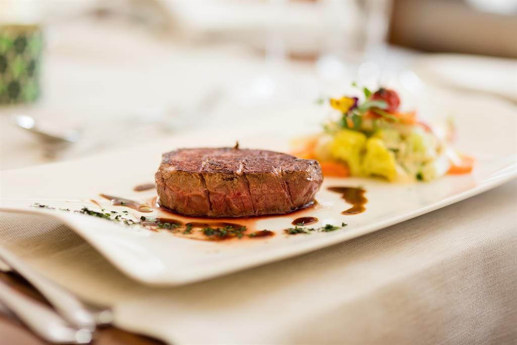 Ein köstliches Stück Rinderfilet auf einem weißen Teller, garniert mit einer Sauce. Neben dem Steak befindet sich ein bunter Gemüsesalat.