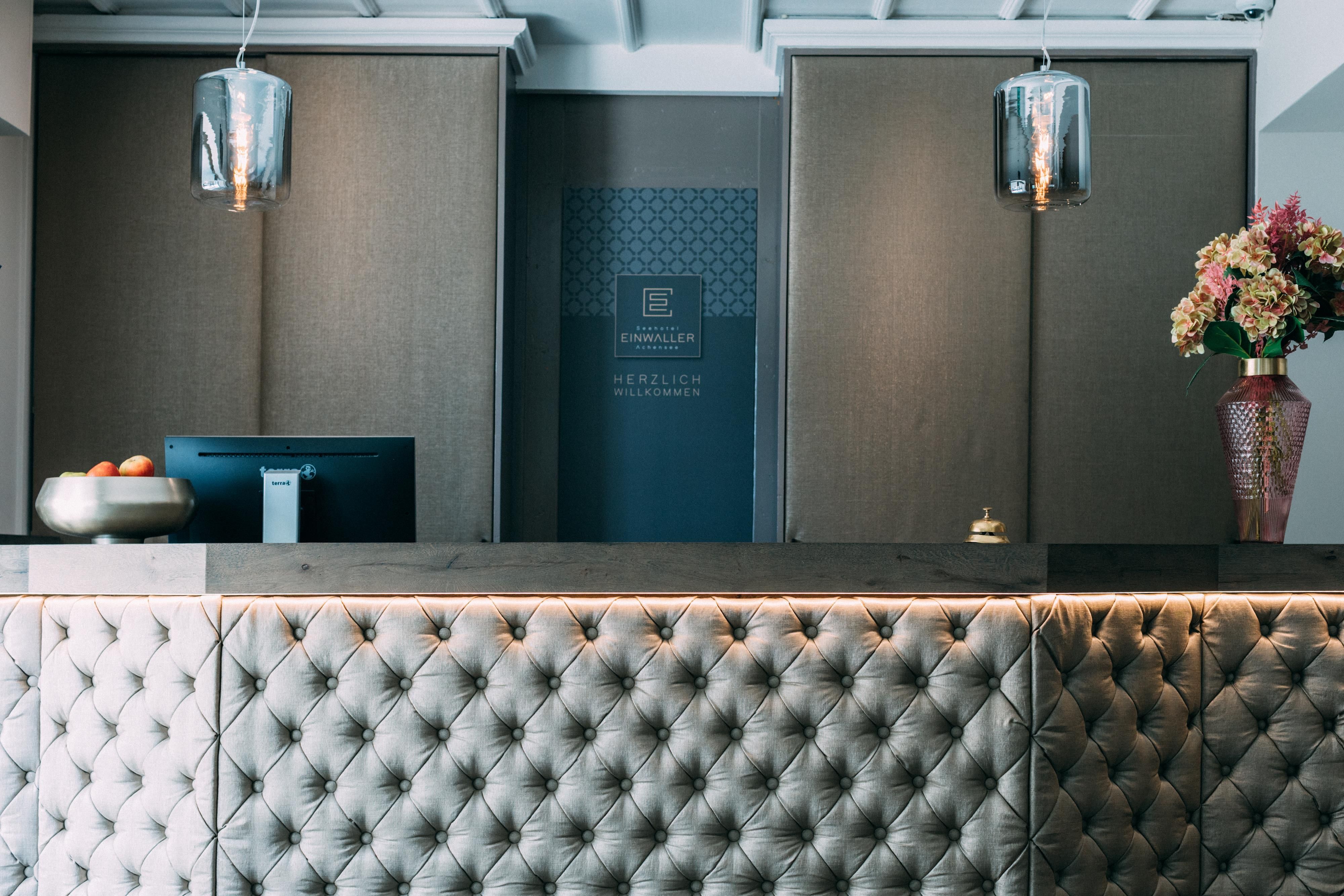 Ein eleganter Rezeptionsbereich mit einem gepolsterten Empfangstresen. Im Hintergrund sind stilvolle Lampen und frische Blumen zu sehen.