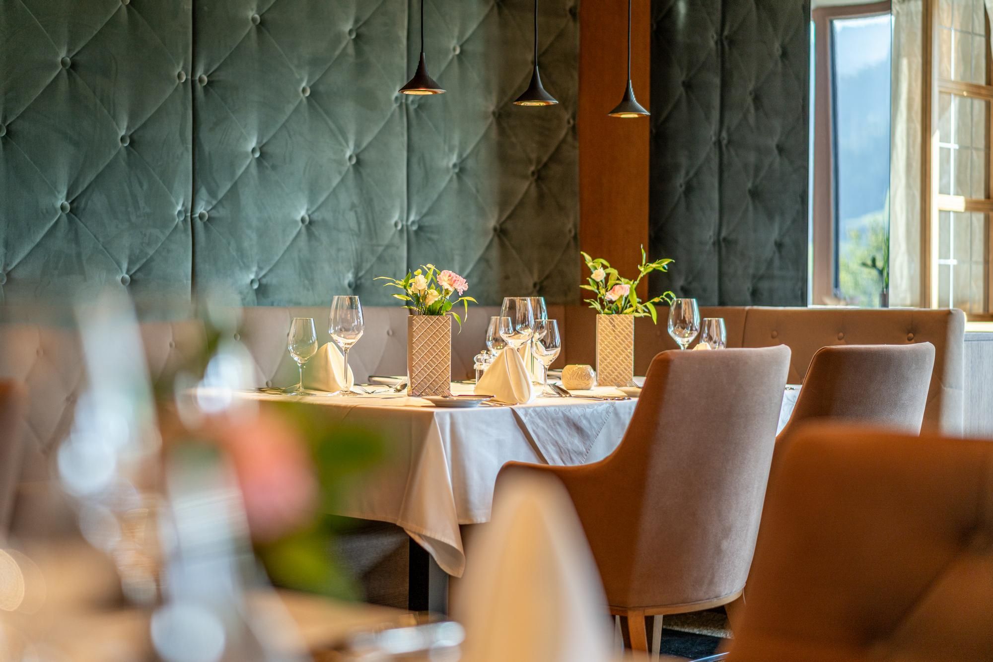 Ein eleganter Restaurantbereich mit schön gedeckten Tischen. Die Wände sind in einem satten Grün gehalten, und kleine Blumenarrangements verschönern die Tische.