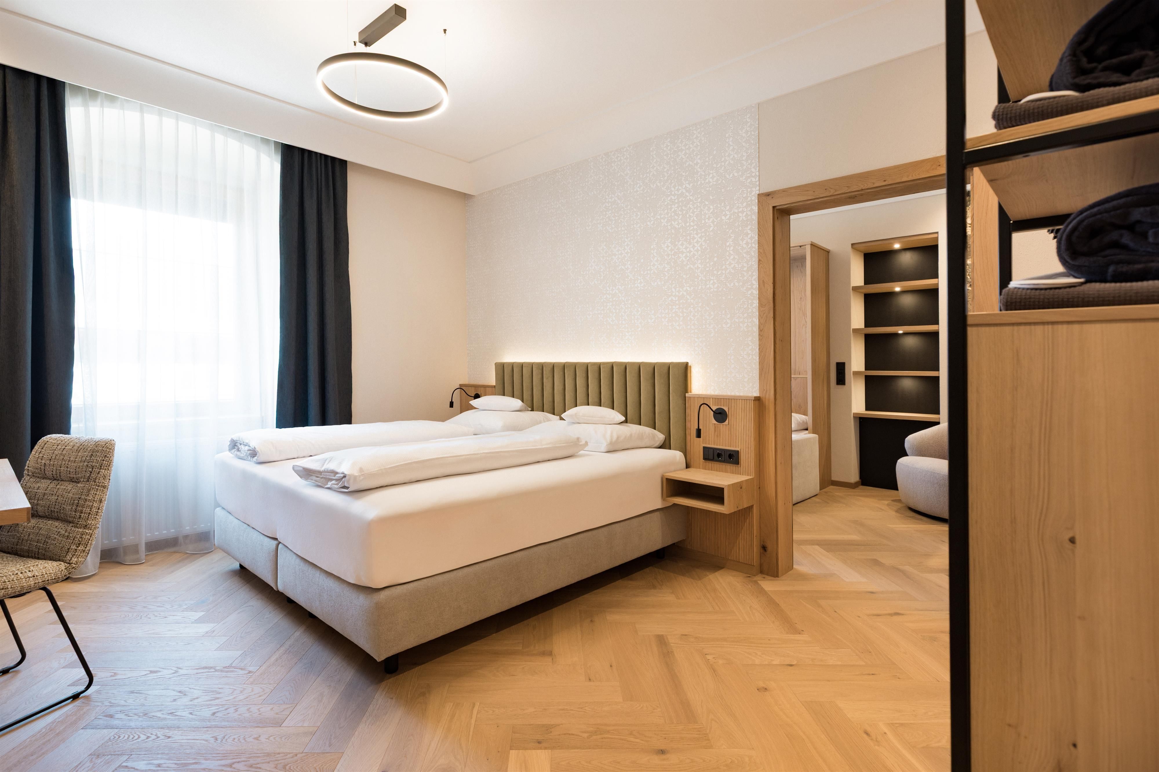 Ein modernes Schlafzimmer mit einem komfortablen Doppelbett und Holzfußboden. Große Fenster sorgen für viel Tageslicht und eine angenehme Atmosphäre.