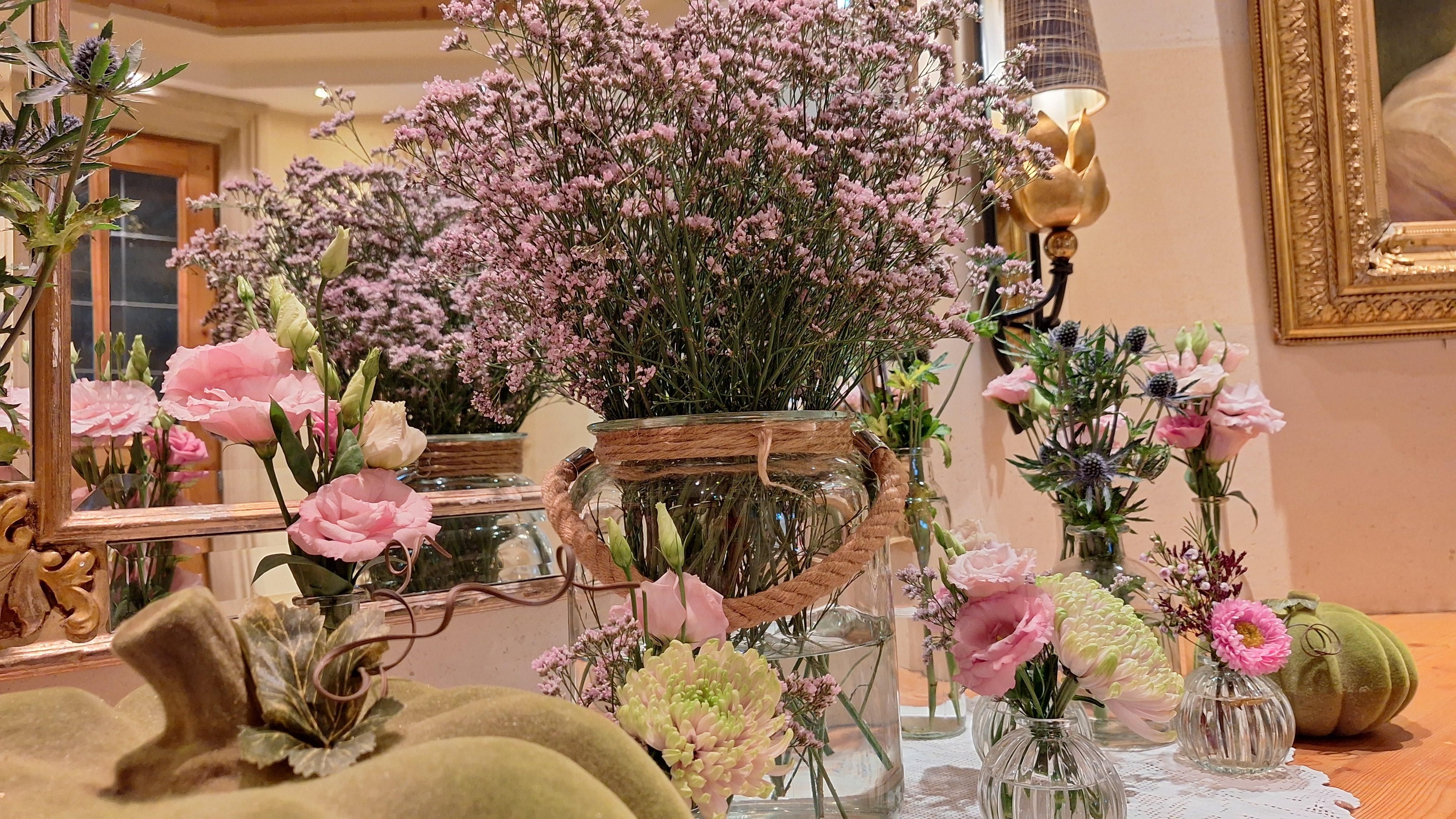 Ein schöner Tisch mit verschiedenen Blumenarrangements in Glasvasen. Die Farben sind sanft und die Atmosphäre wirkt einladend.