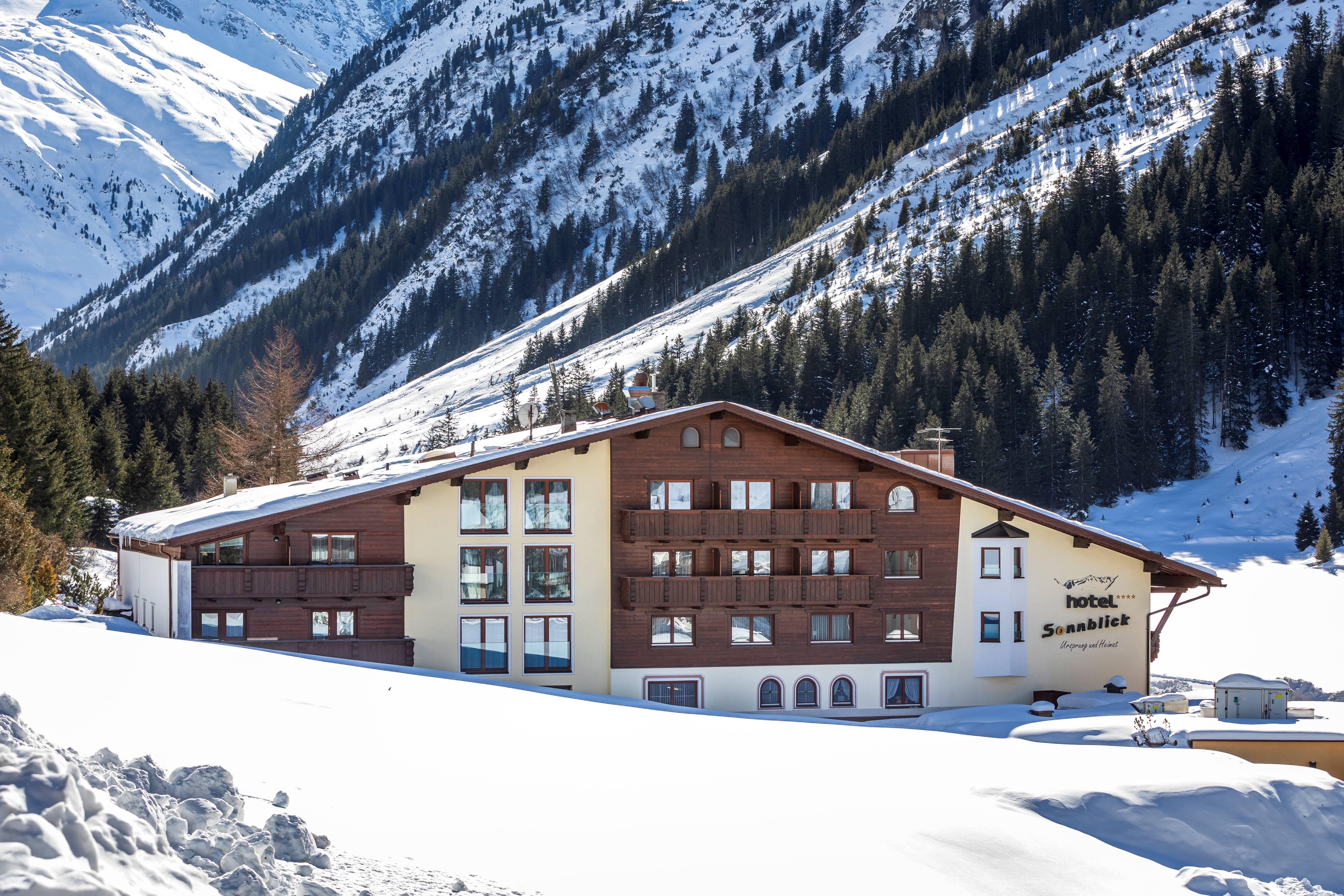 Ein stilvolles Hotel inmitten einer verschneiten Berglandschaft. Die Umgebung ist geprägt von hohen Tannen und majestätischen Bergen.