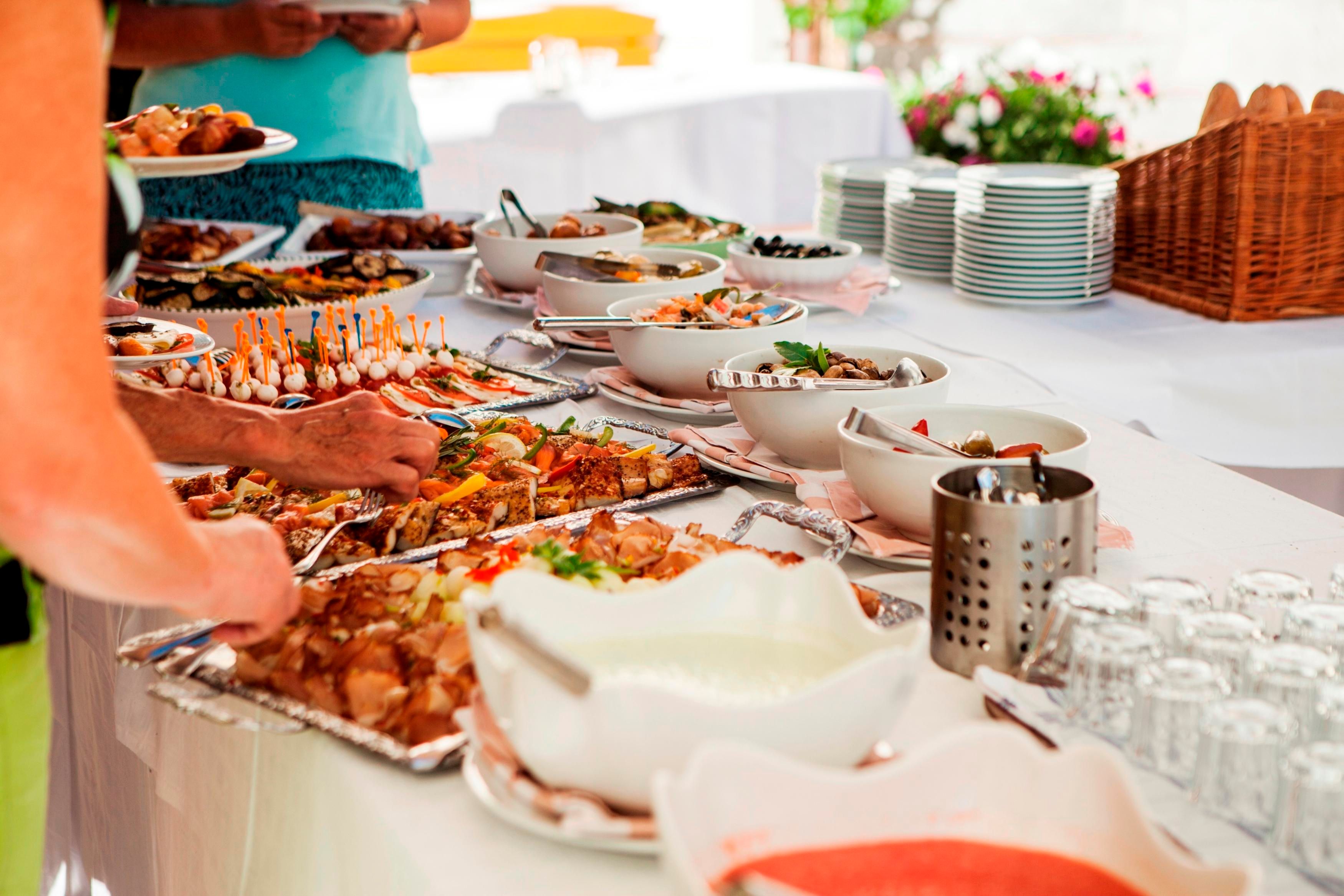 Ein reichhaltiges Buffet mit verschiedenen Gerichten und Salaten. Im Hintergrund sind einige Blumen und Geschirr zu sehen.