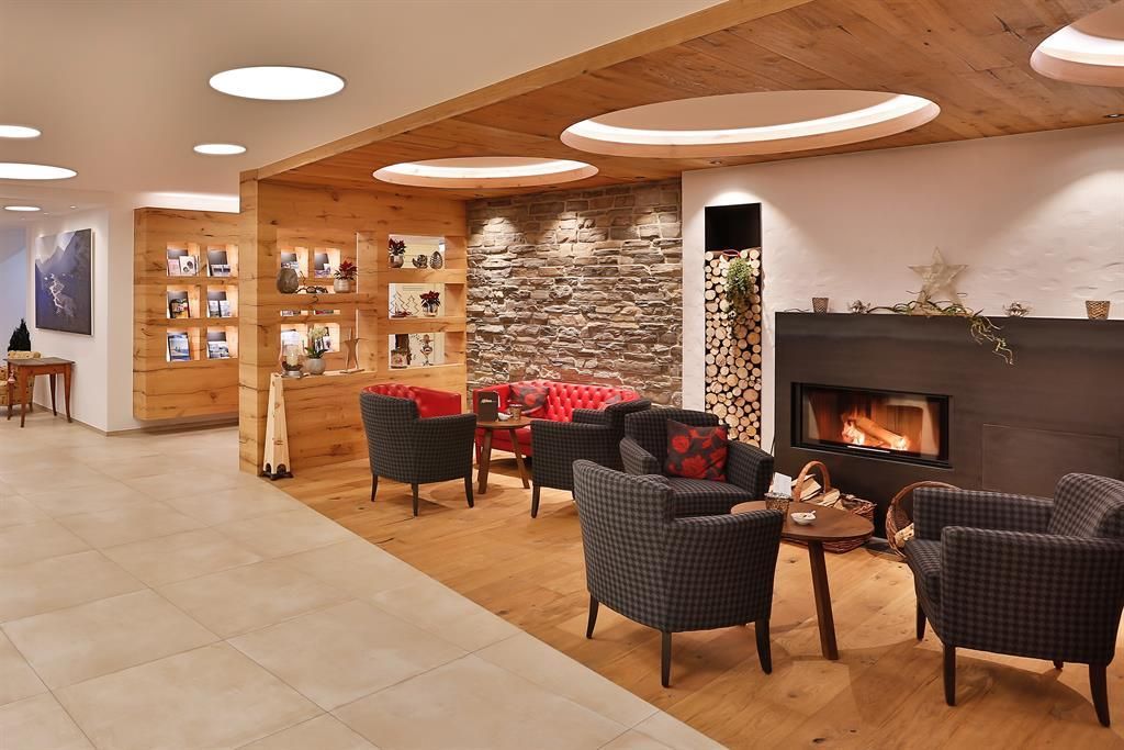 Eine gemütliche Lounge mit einem offenem Kamin und modernen Möbeln. Die Wände sind mit Holz und Steinen dekoriert, und es gibt eine einladende Atmosphäre.