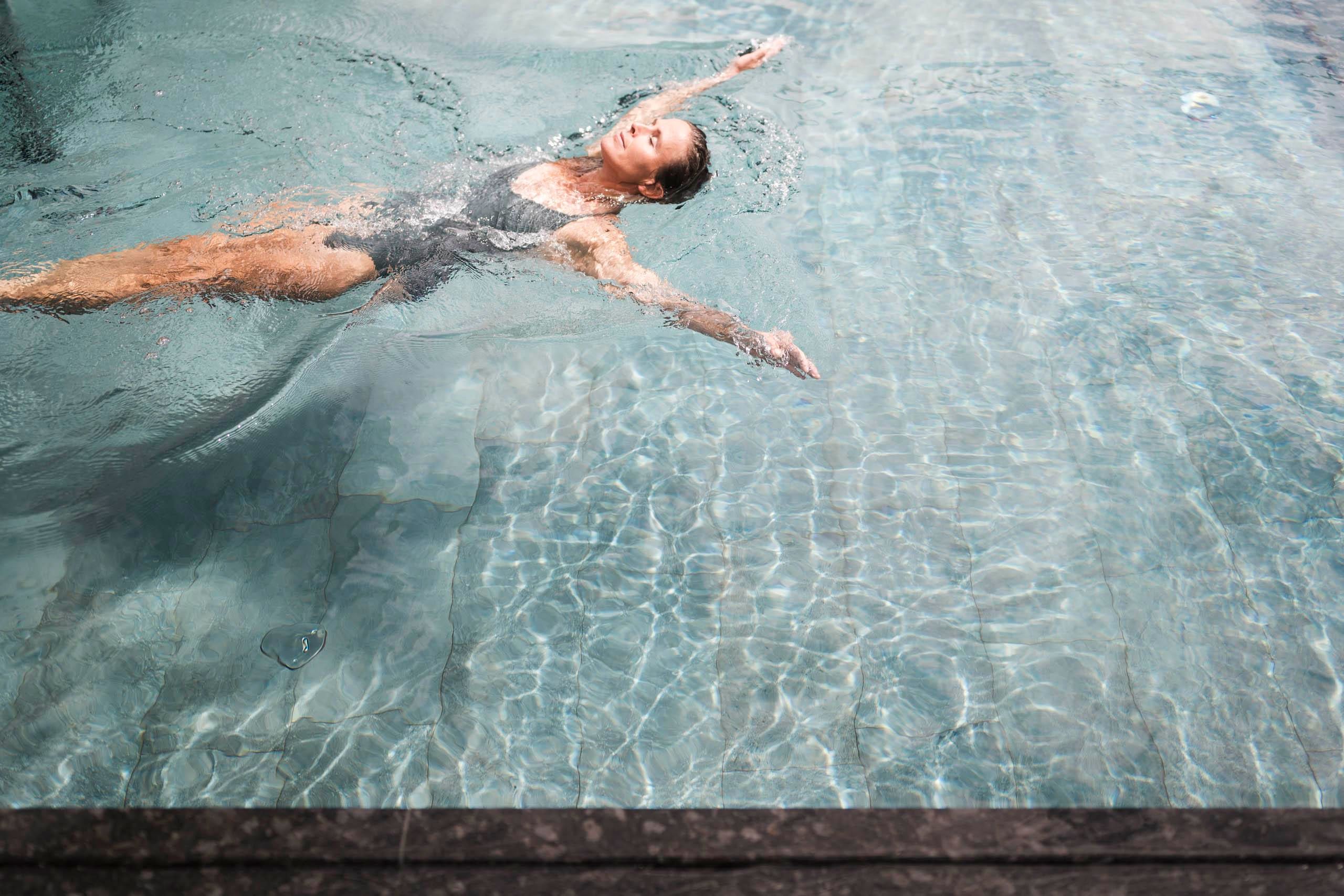 Eine Frau schwimmt entspannt in einem klaren Pool. Das Wasser reflektiert sanft das Licht und sorgt für eine ruhige Atmosphäre.