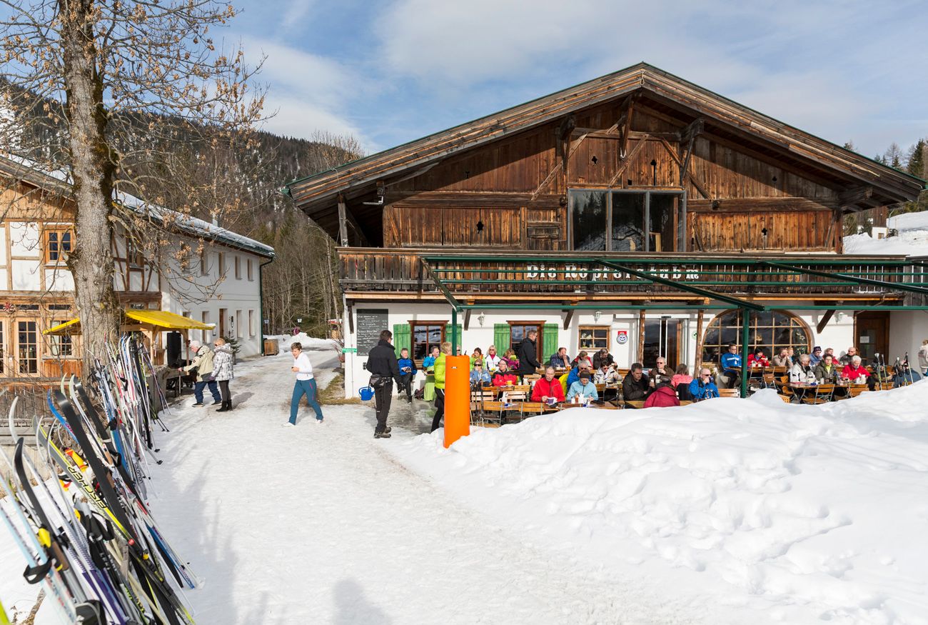 Altes Gasthaus mit gut besuchter Sonnenterrasse, viele Langlaufski lehnen am Zaun
