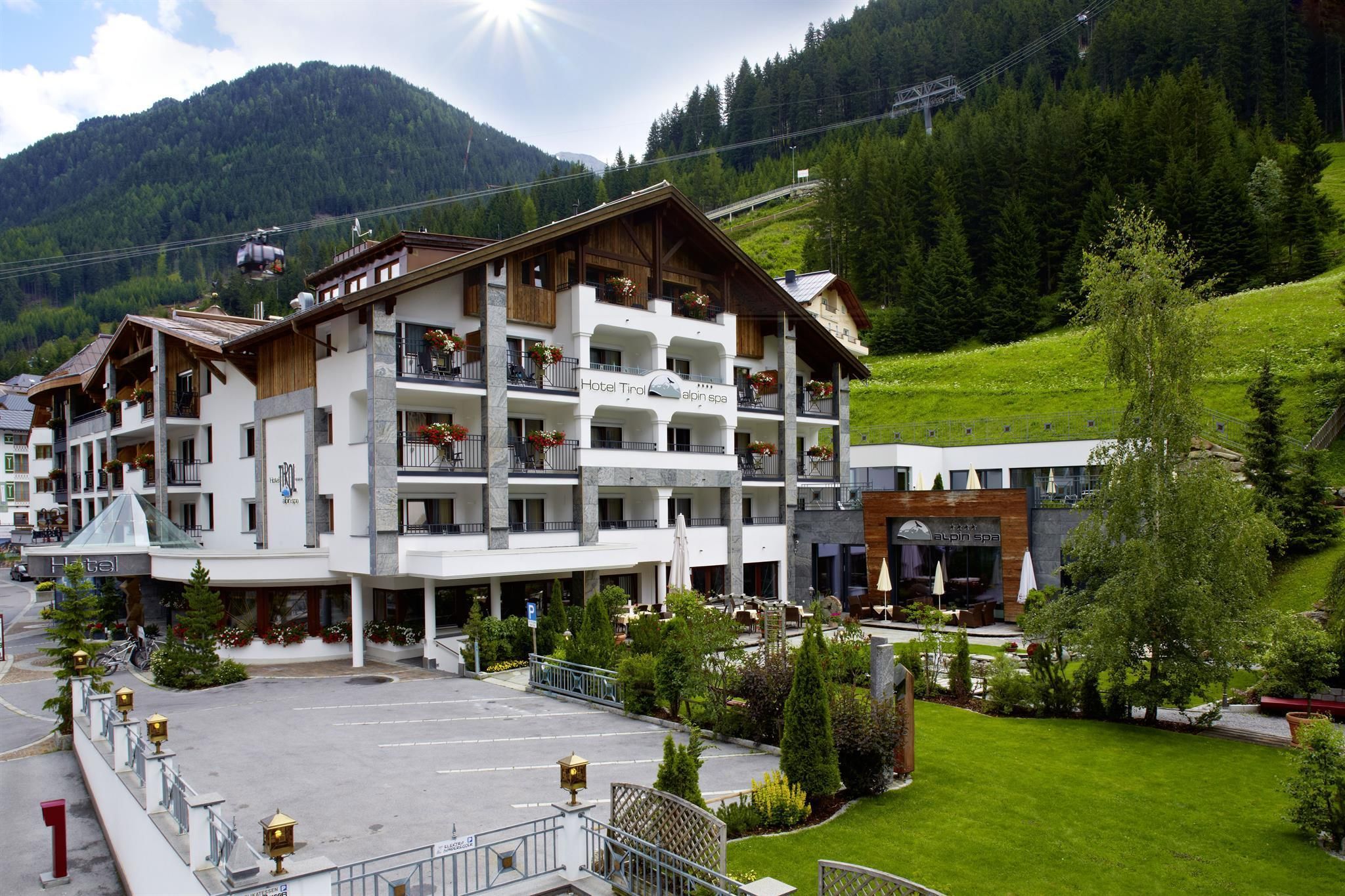 Ein modernes Hotel in den Bergen mit grünem Rasen und schönen Bäumen. Im Hintergrund sind die Landschaft und die Berge zu sehen.