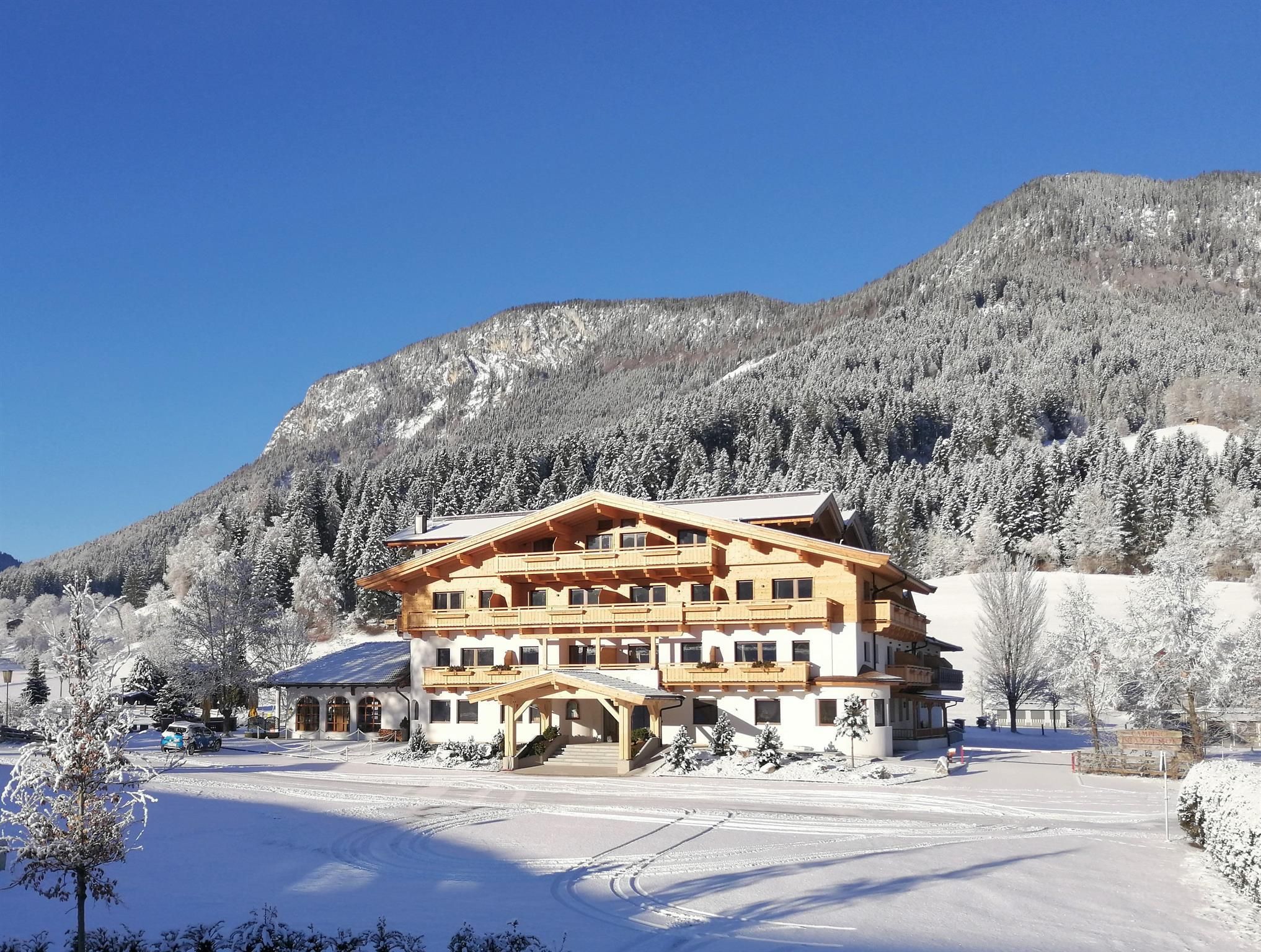Ein charmantes Hotel im Winter, umgeben von schneebedeckten Bergen und Bäumen. Der klare blaue Himmel sorgt für eine beruhigende Stimmung.