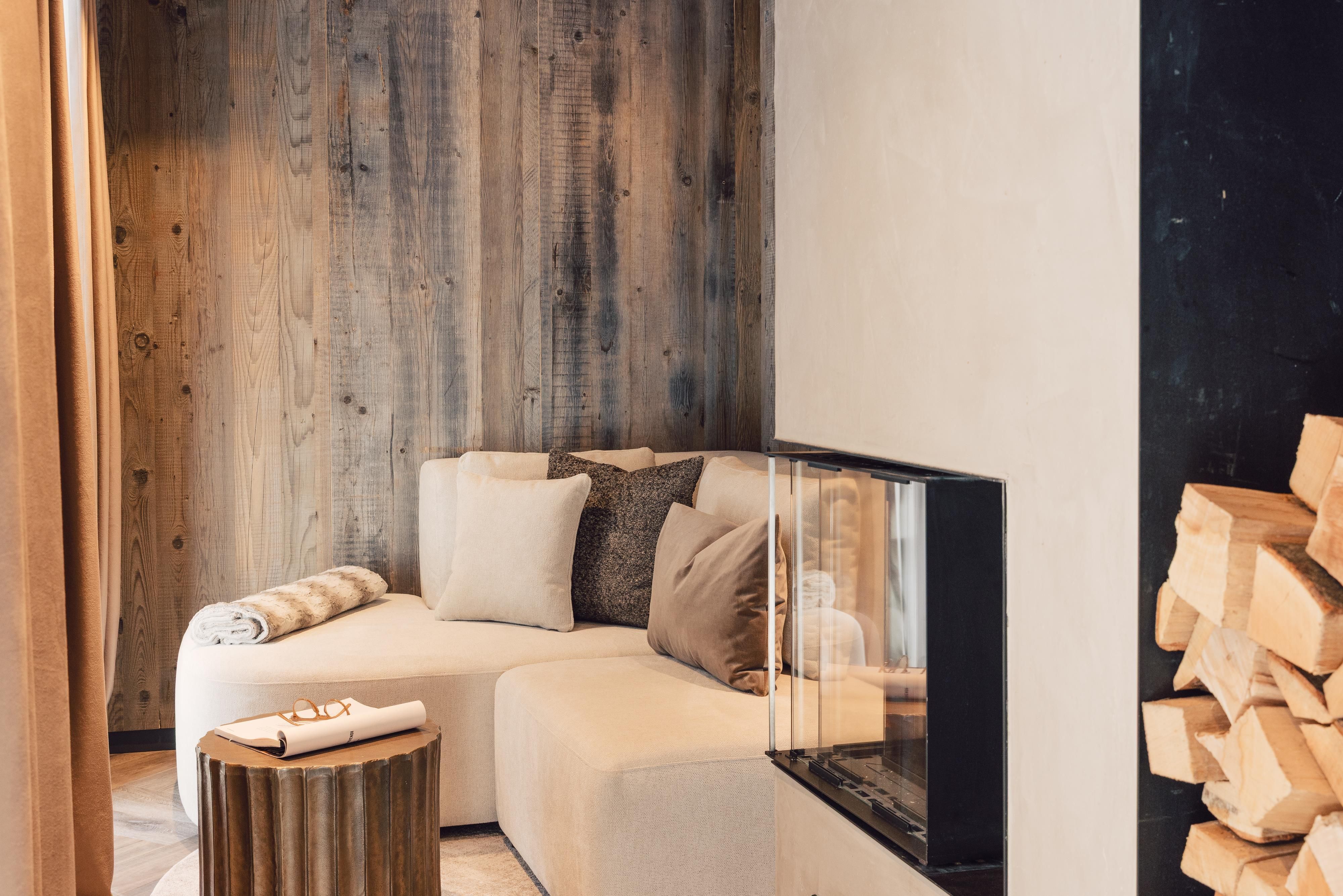 Ein elegantes Wohnzimmer mit einem bequemen, L-förmigen Sofa und einem modernen Kamin. Holzverkleidete Wände schaffen eine gemütliche Atmosphäre.