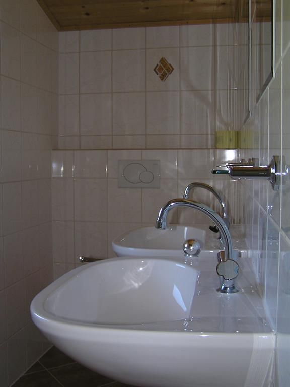 Ein modernes Badezimmer mit zwei Waschbecken und eleganten Wasserhähnen. Die Wände sind gefliest und die Einrichtung ist funktional.