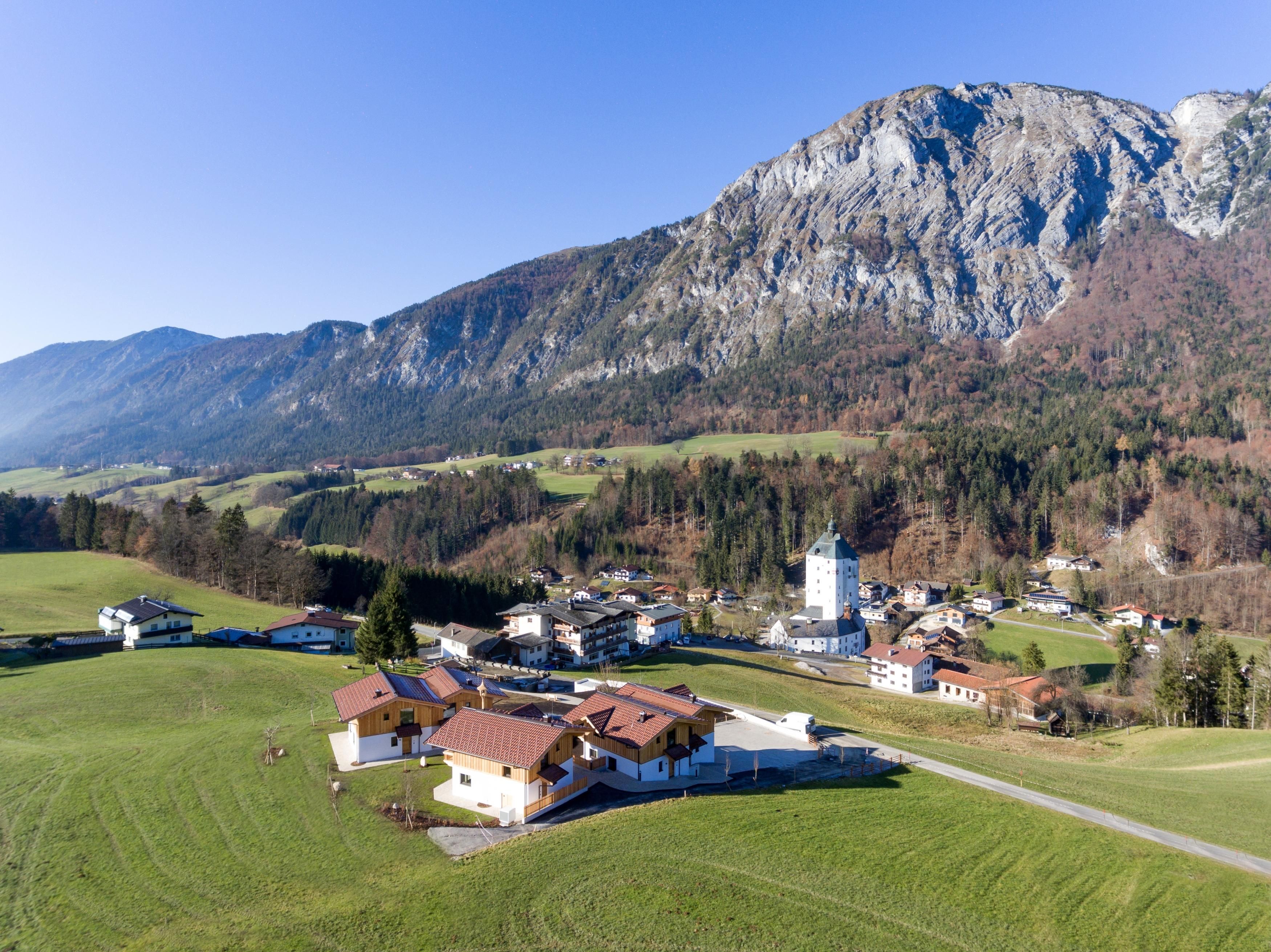 Eine malerische Landschaft mit einem kleinen Dorf inmitten von grünen Wiesen und bewaldeten Bergen. Im Hintergrund erhebt sich ein beeindruckender Berg.
