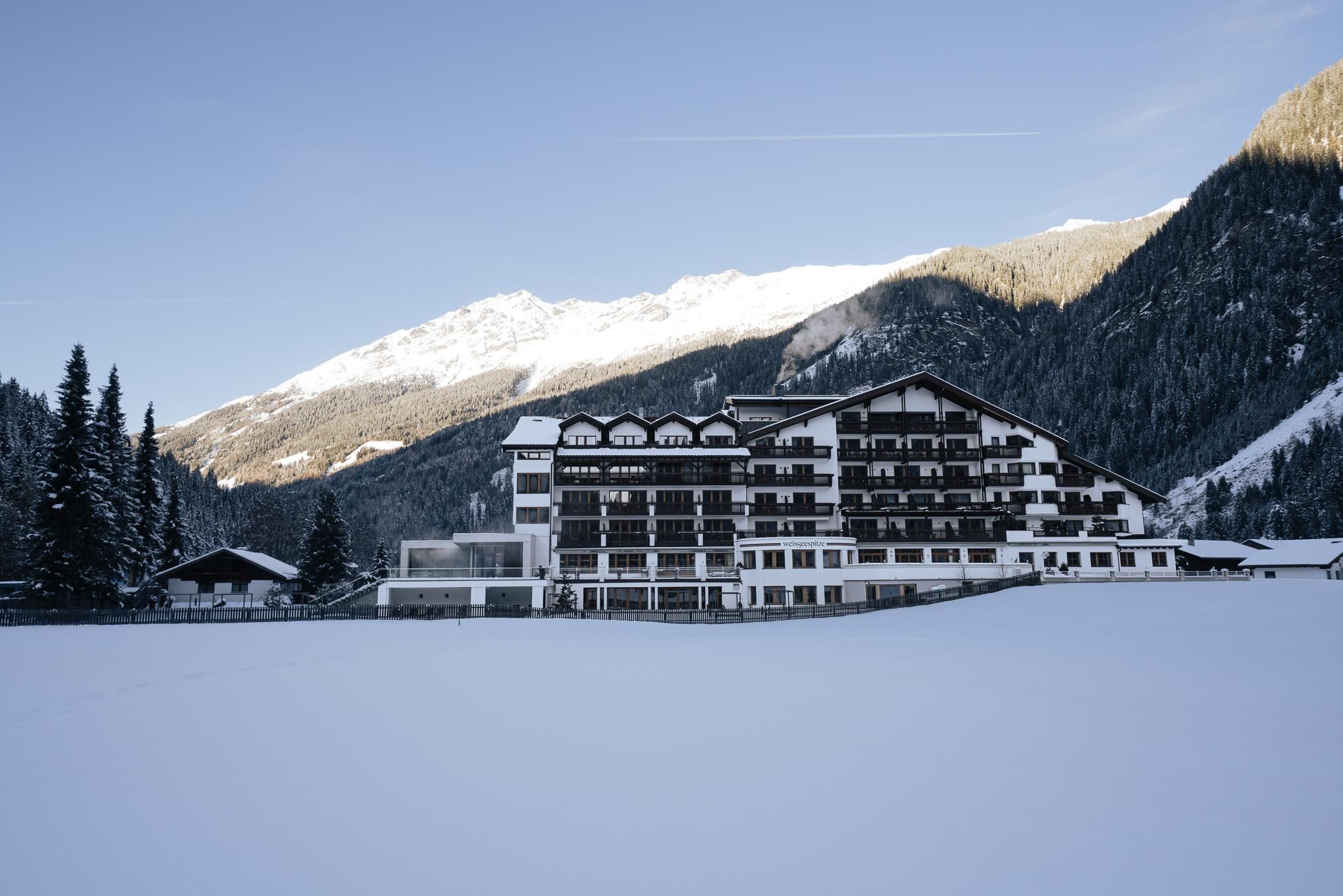 Ein schneebedecktes Hotel in den Bergen. Die Umgebung ist ruhig und malerisch, umgeben von hohen Tannen und majestätischen Bergen.