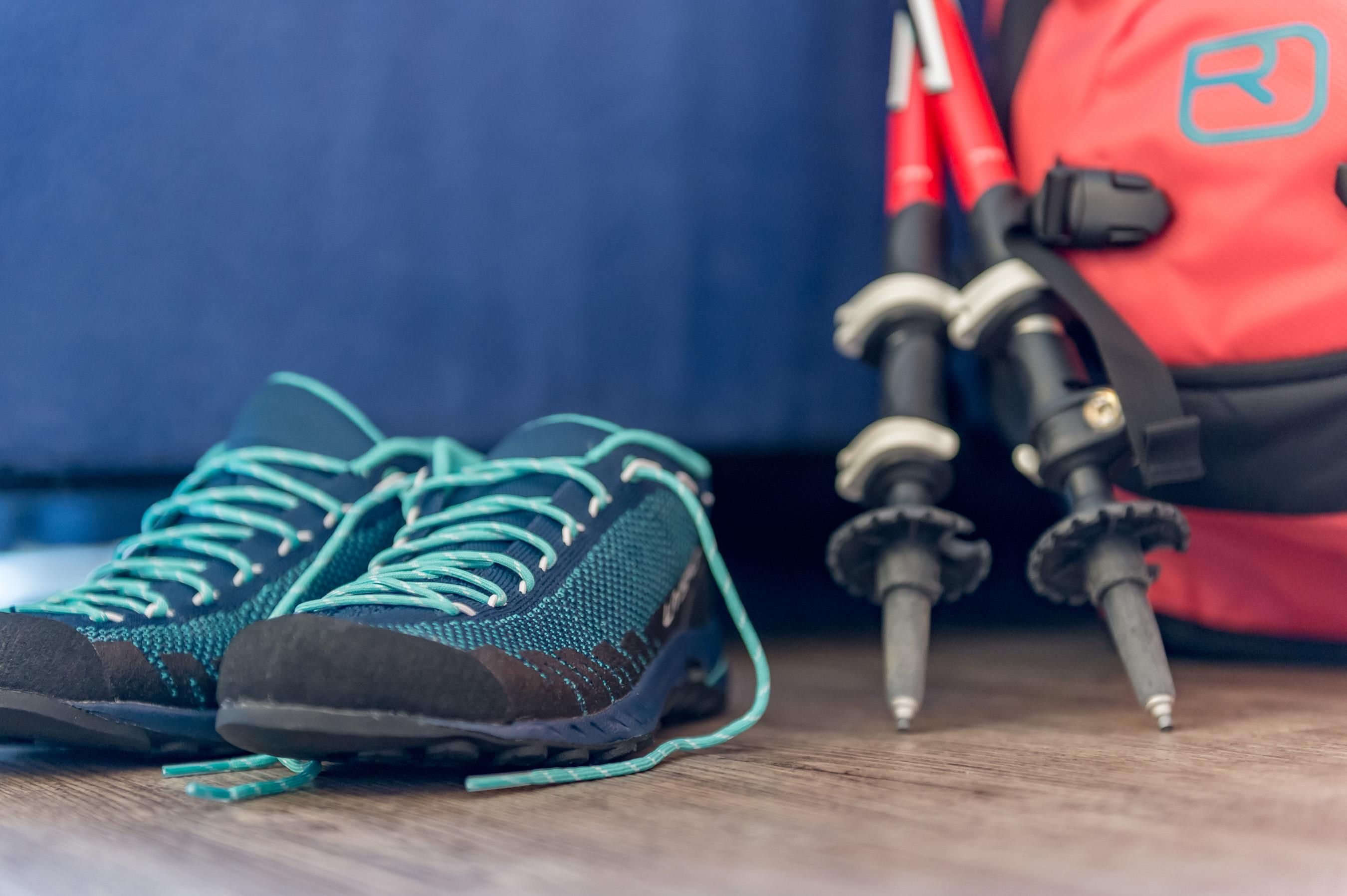 Wander- und Trekkingausrüstung liegt bereit. Neben einem Rucksack stehen Schuhe und Wanderstöcke.