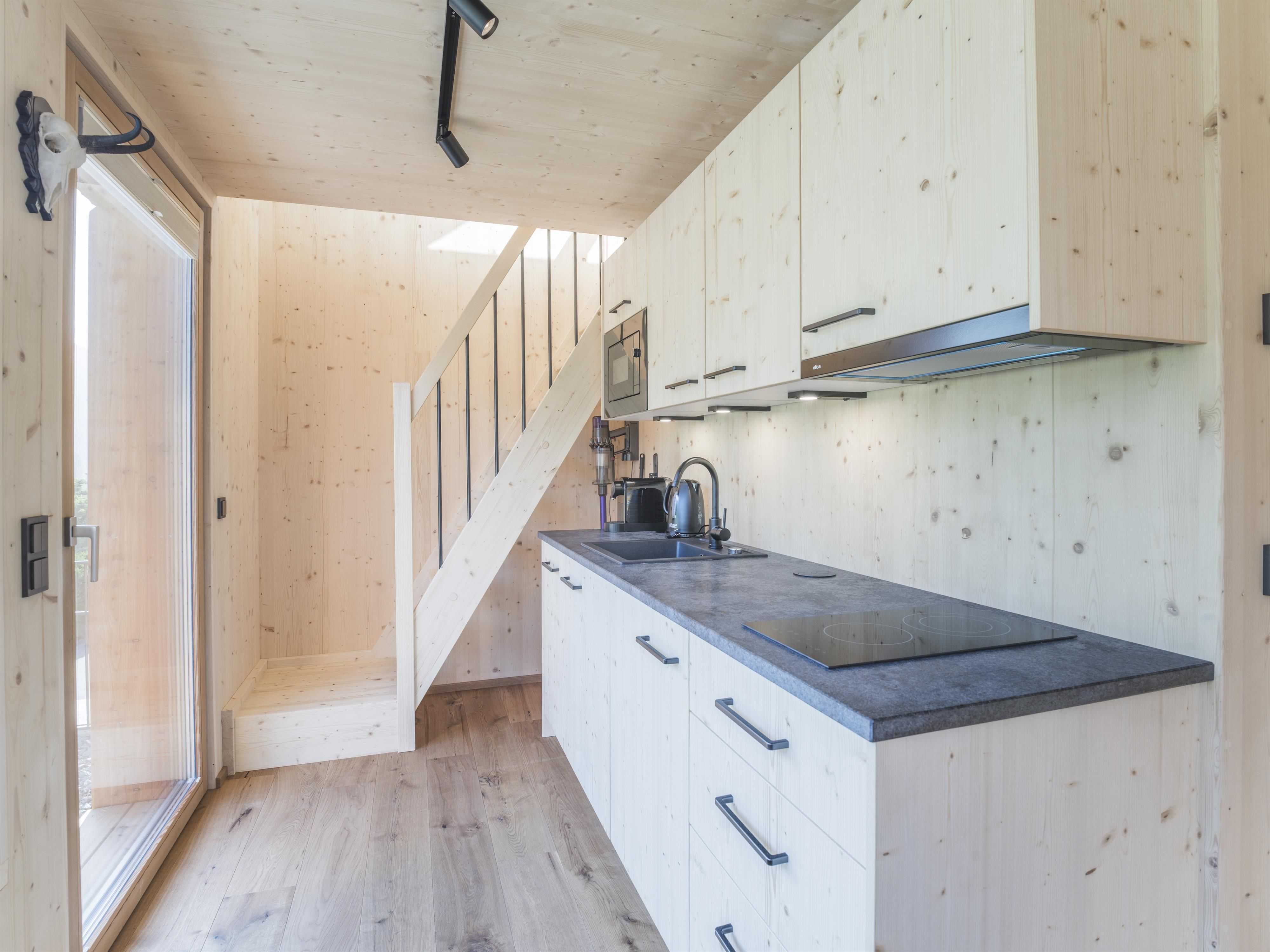 Eine moderne Küche mit hellen Holzschränken und einem schwarzen Kochfeld. Eine Treppe führt zu einem oberen Bereich.