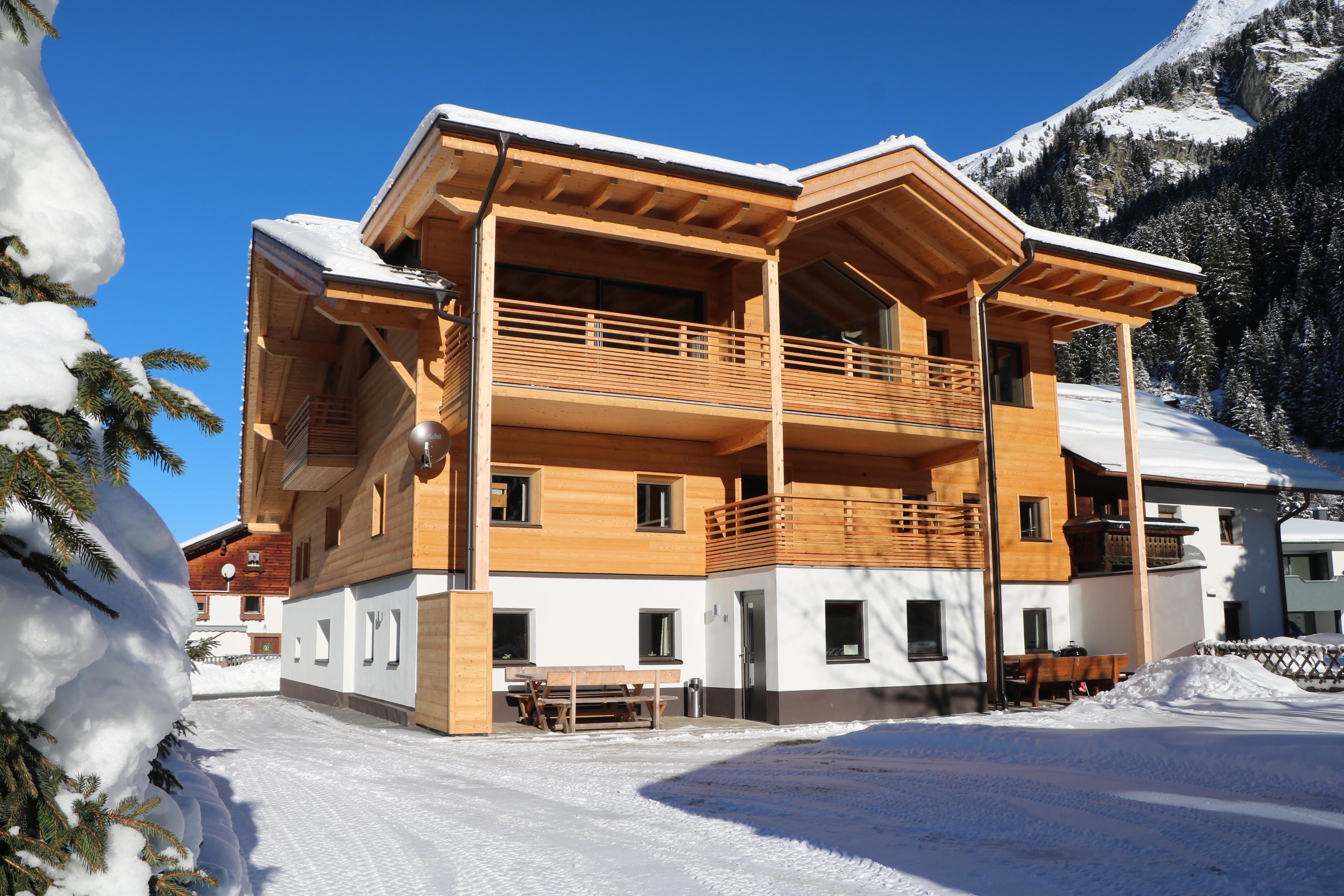 Ein modernes Holzhaus in einer schneebedeckten Landschaft. Die klare Winterluft und die Berge im Hintergrund schaffen eine gemütliche Atmosphäre.