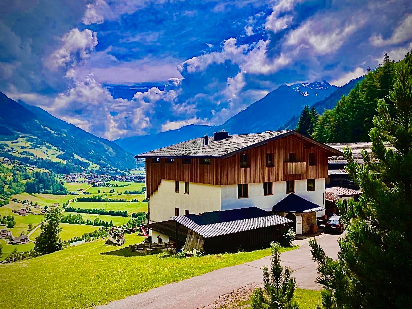 Ein malerisches Haus in den Bergen, umgeben von grünen Wiesen und majestätischen Gipfeln. Der Himmel ist blau und mit einigen Wolken durchzogen.Ausblick nach Matrei