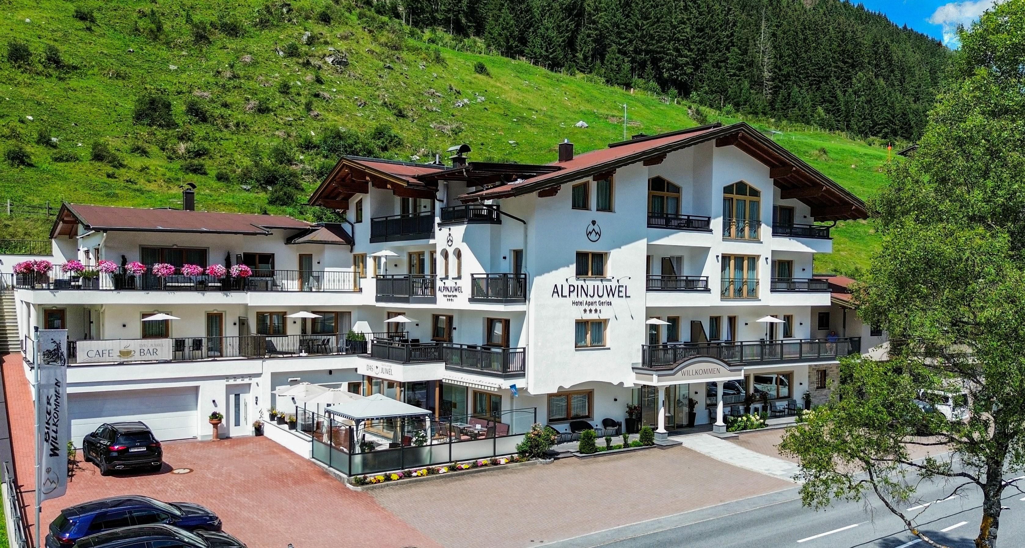 Ein schönes Hotel mit Alpenblick und grünem Hintergrund. Es hat eine einladende Terrasse und oberhalb der Straße liegt ein Parkplatz.
