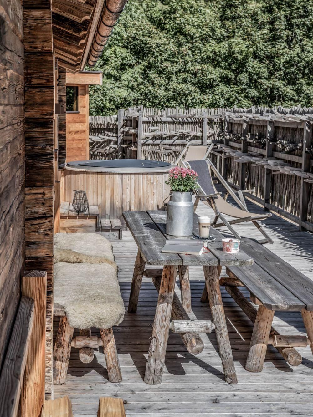 Eine gemütliche Terrasse mit rustikalen Holzmöbeln und einer Holzbadewanne. Die Umgebung ist grün und lädt zum Entspannen ein.