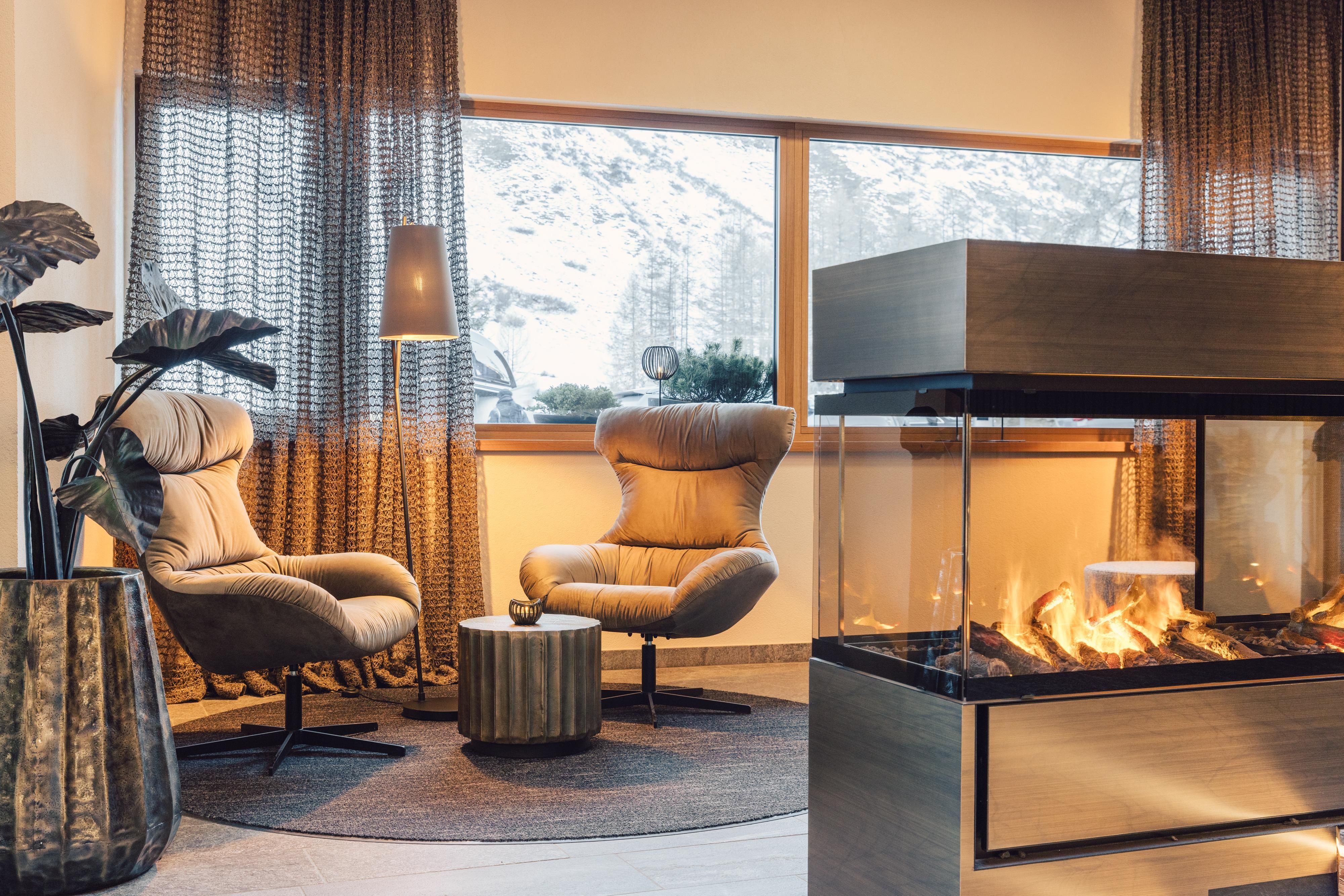 Ein gemütlicher Raum mit zwei bequemen Sesseln und einem modernen Kamin. Die großen Fenster bieten einen schönen Blick auf die schneebedeckte Landschaft.