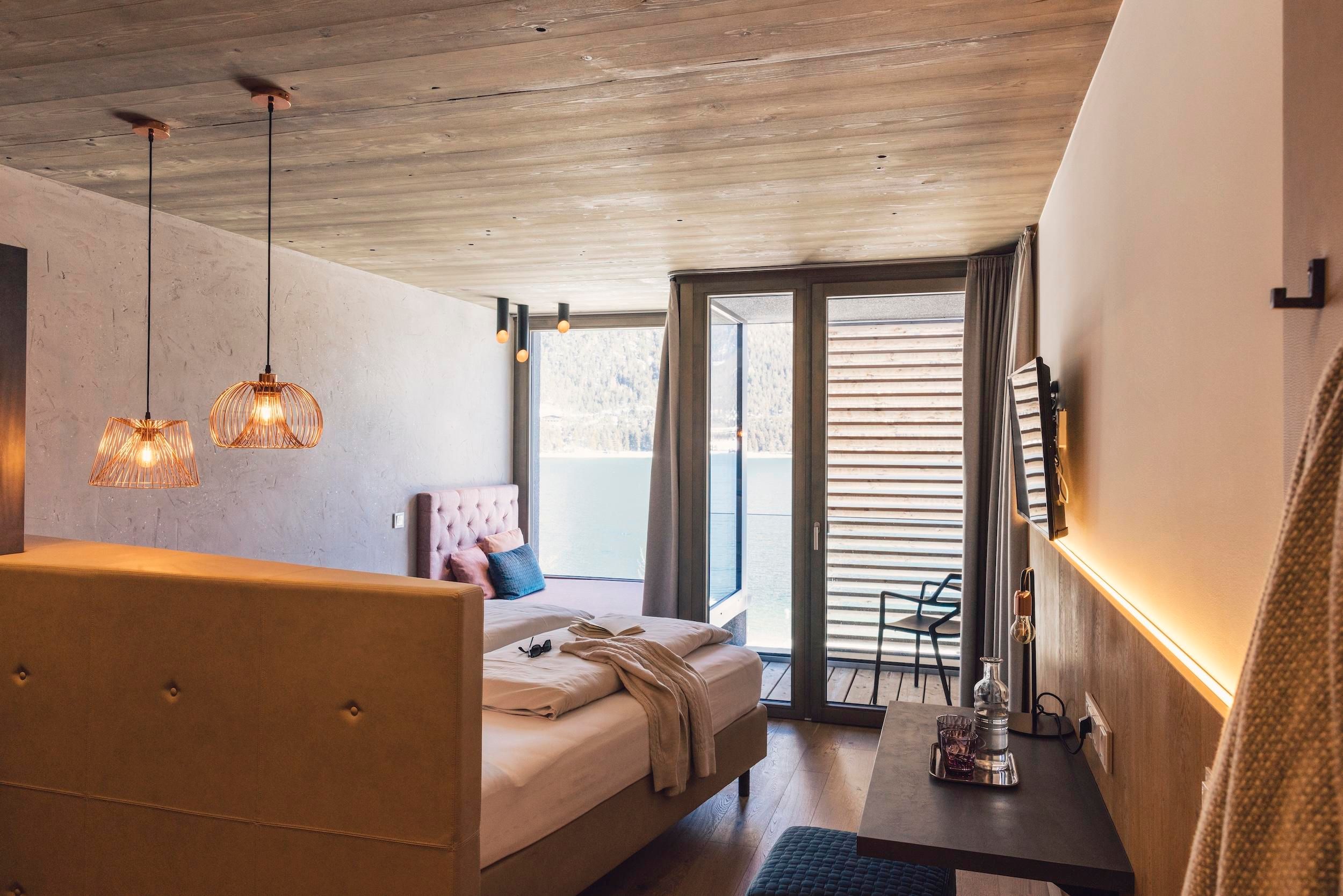 Ein modernes Zimmer mit einem großen Bett und Zugang zu einem Balkon. Die Einrichtung ist stilvoll mit warmen Lichtakzenten und einer angenehmen Atmosphäre.