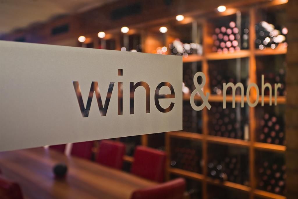Ein eleganter Weinkeller mit Glasfenster und gut gefüllten Weinschränken. Der Tisch im Vordergrund ist für eine intime Verkostung vorbereitet.