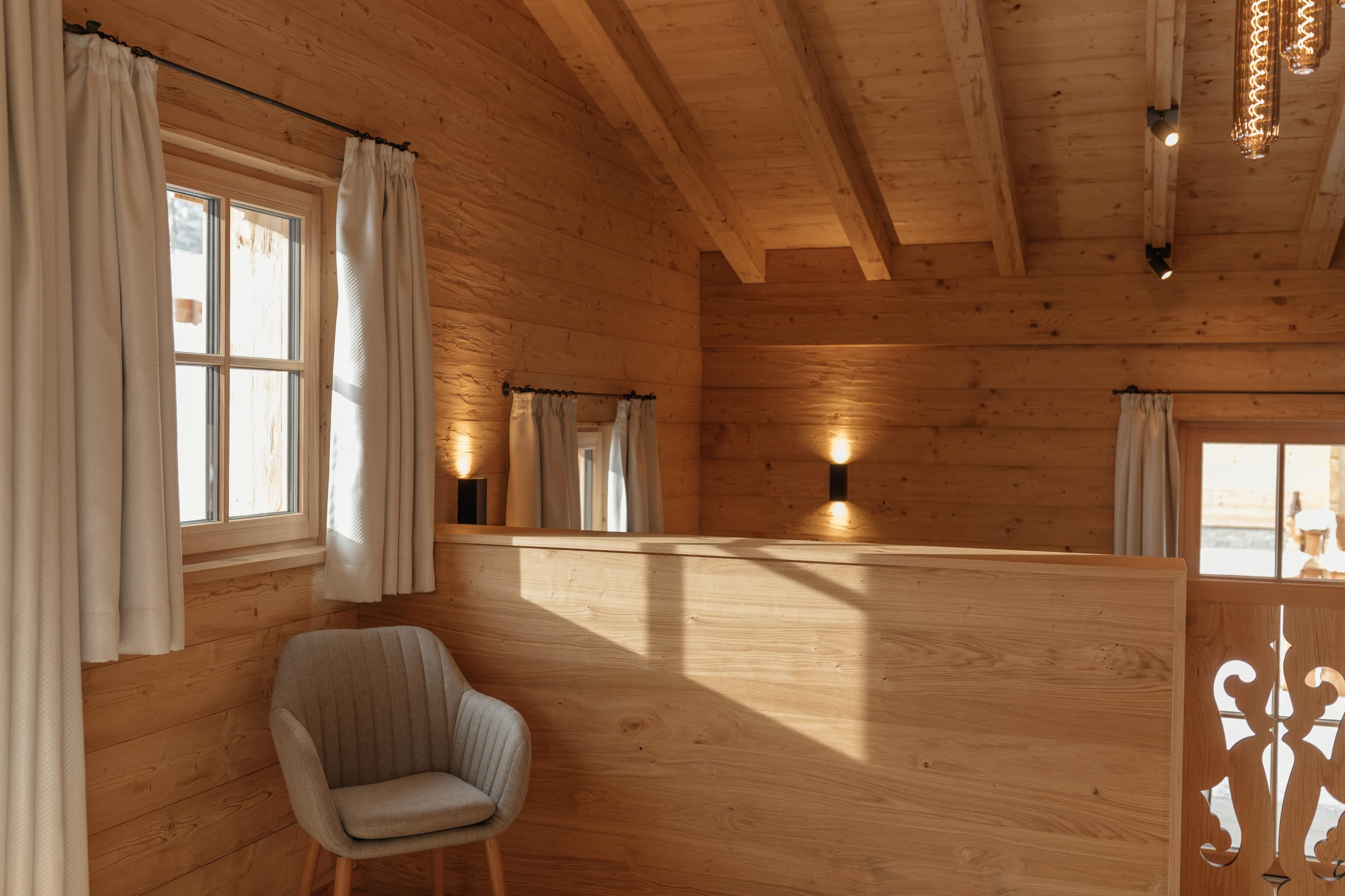 Ein gemütlicher Raum mit Holzverkleidung und großen Fenstern. Ein moderner Stuhl und sanfte Beleuchtung schaffen eine einladende Atmosphäre.