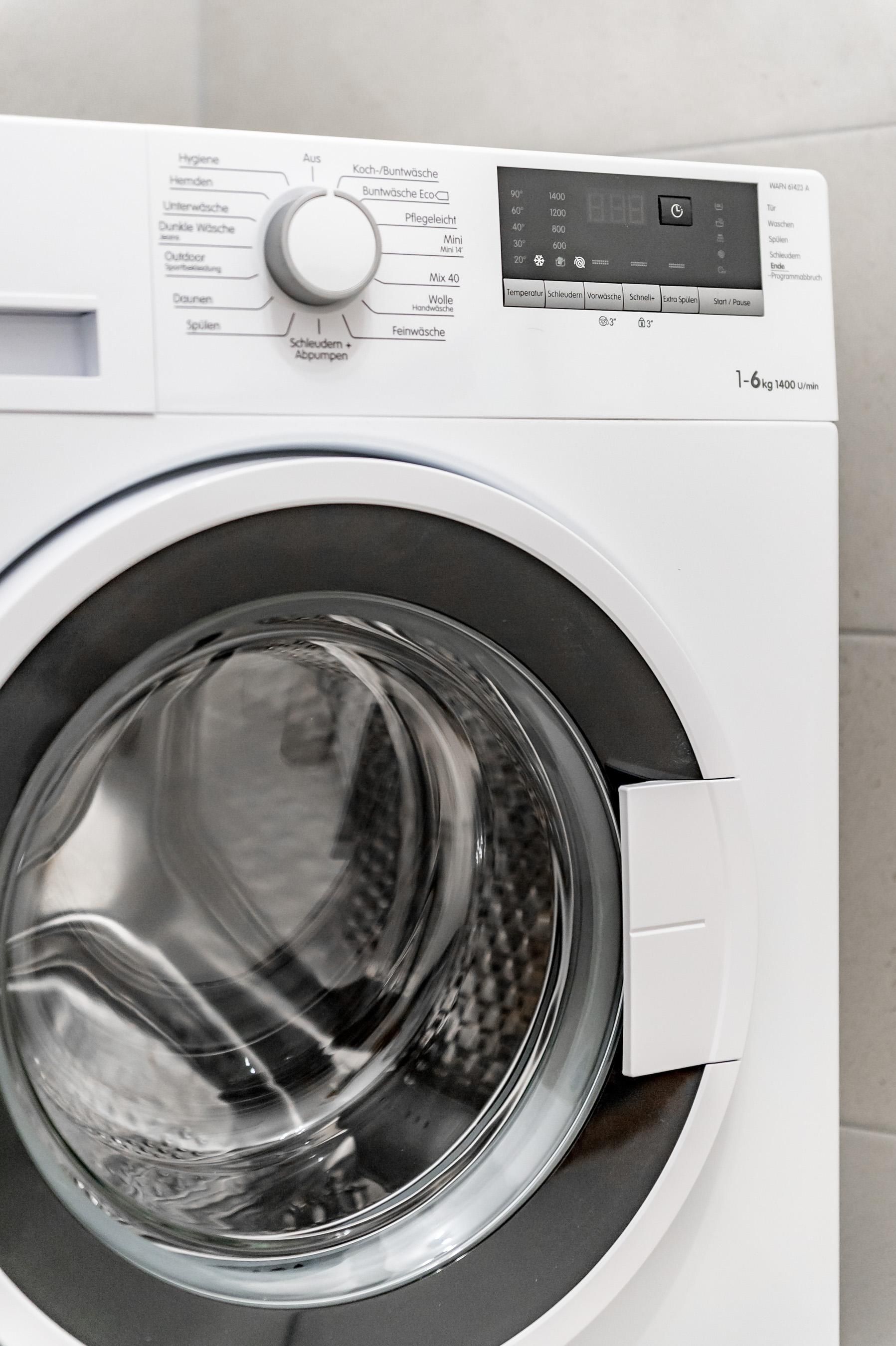 Eine moderne Waschmaschine mit einem runden Bullauge. Sie steht in einem hellen Raum.
