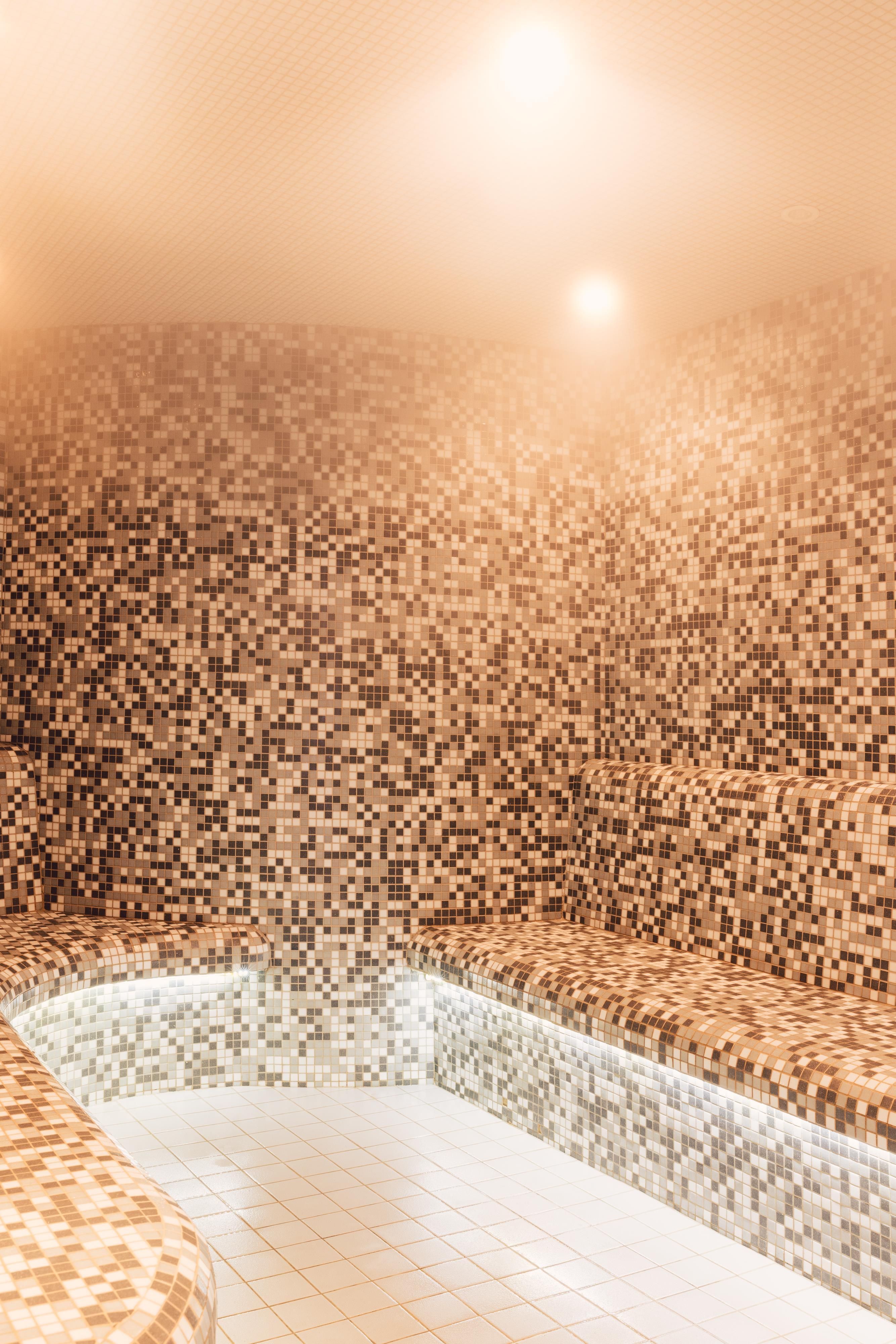 Ein modernes Dampfbad mit mosaikverzierten Wänden und Bänken. Sanftes Licht schafft eine entspannende Atmosphäre.