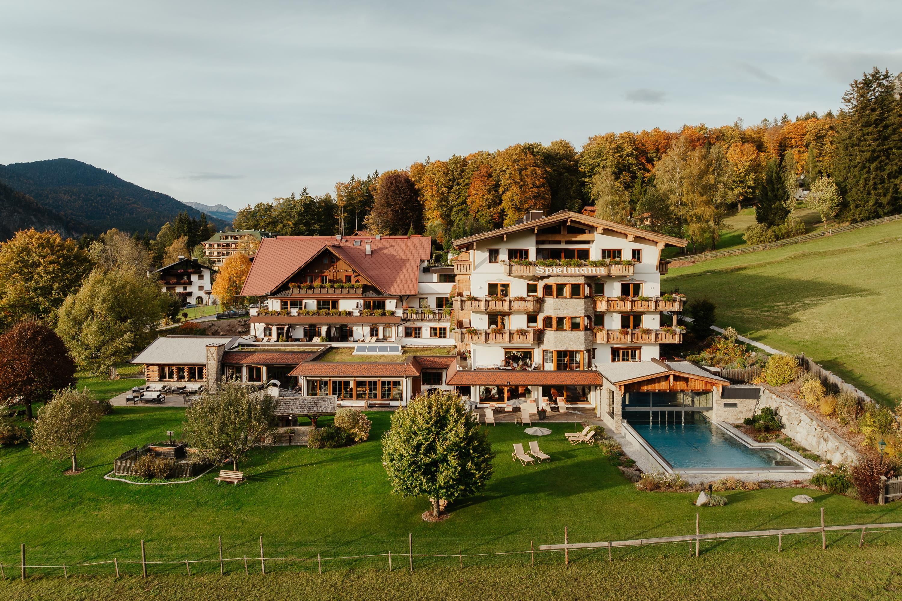 Ein schönes Hotel in einer malerischen Landschaft mit bunten Bäumen im Hintergrund. Es gibt einen Pool und gepflegte Gartenanlagen.