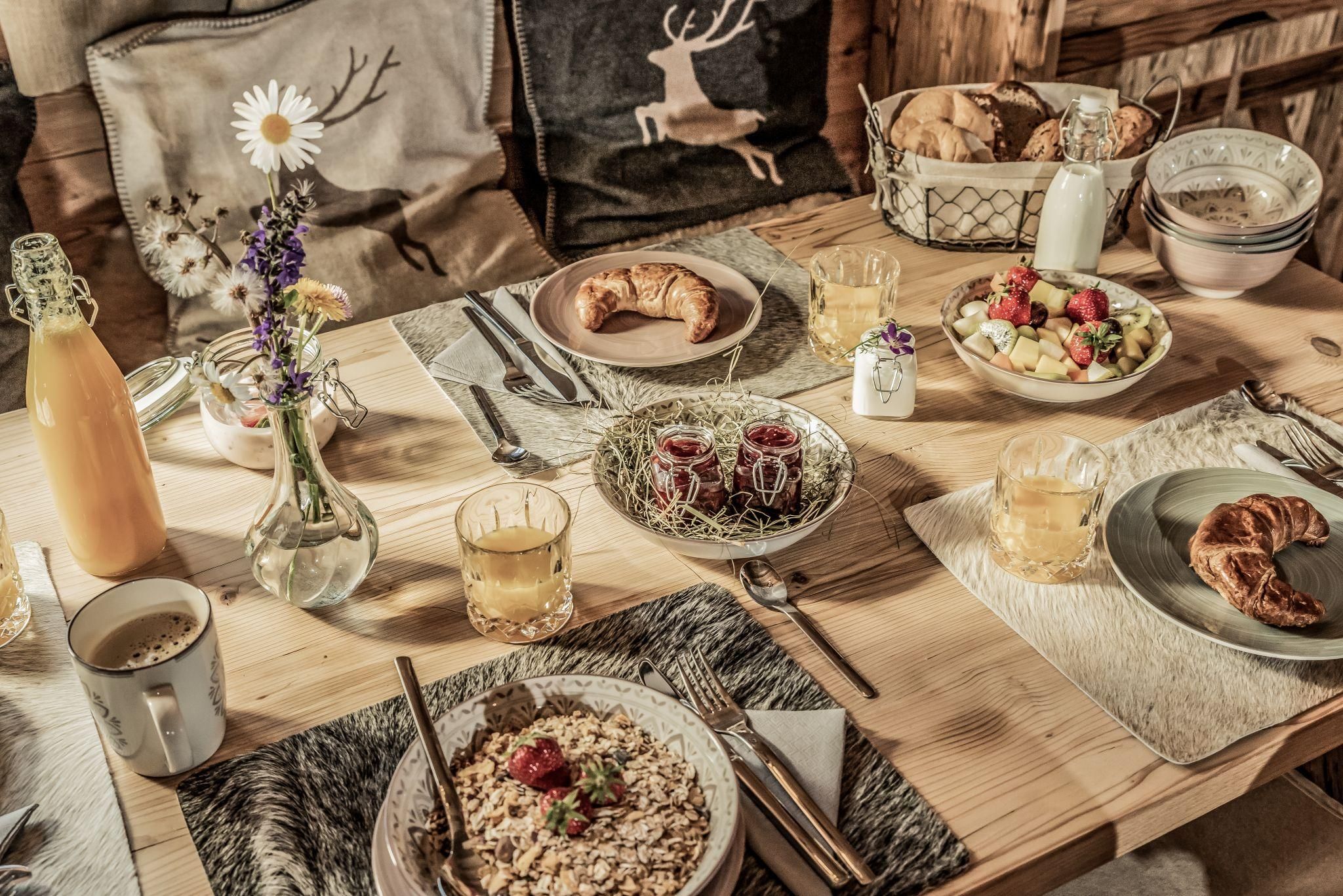 Ein einladender Frühstückstisch mit verschiedenen Speisen, darunter Croissants, Joghurt und frisches Obst. Auf dem Tisch stehen auch Getränke und Blumenarrangements, die eine gemütliche Atmosphäre schaffen.