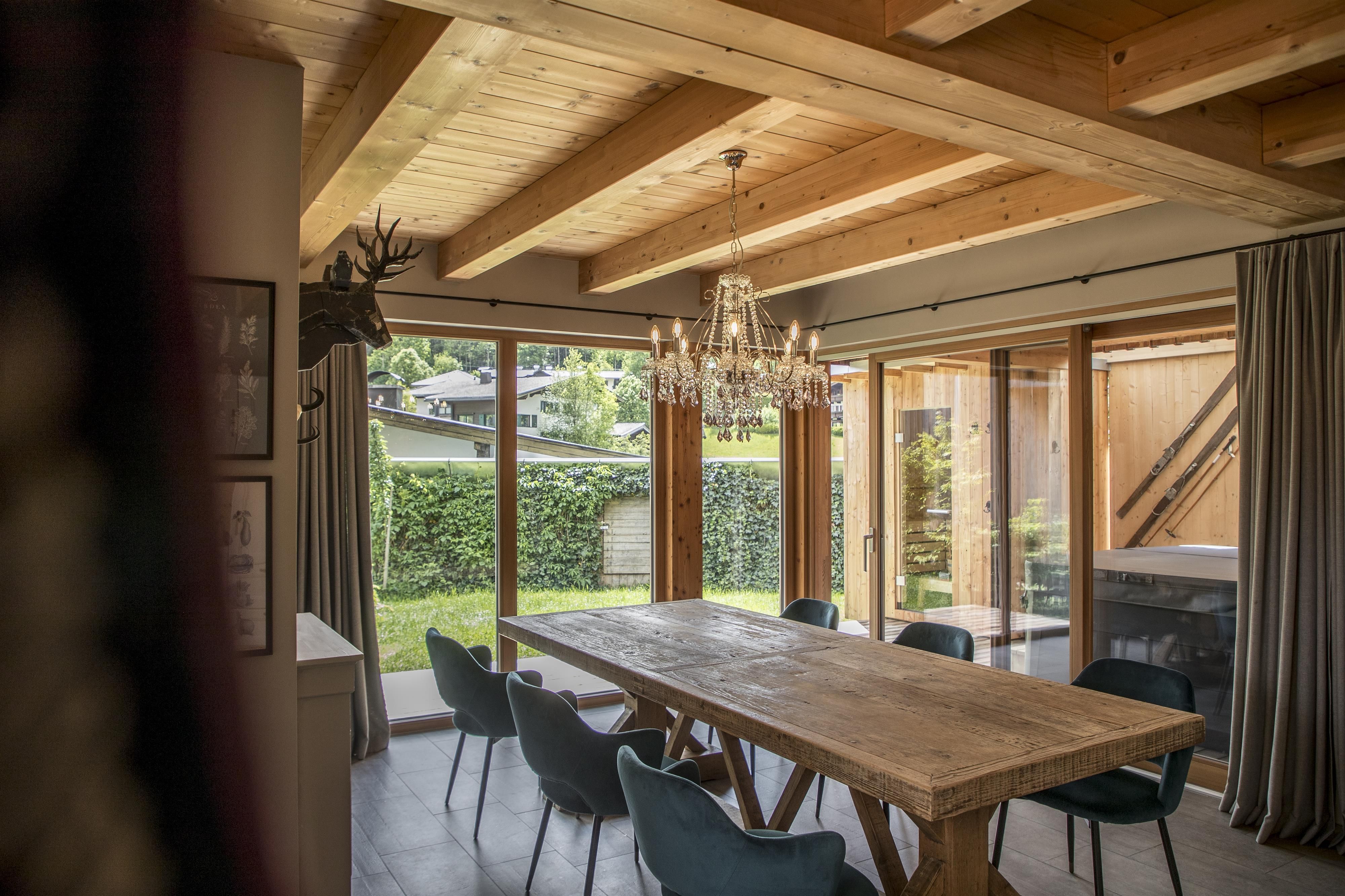 Ein einladender Essbereich mit einem großen Holztisch und modernen Stühlen. Große Fenster bieten Ausblick auf den Garten und lassen viel Tageslicht herein.