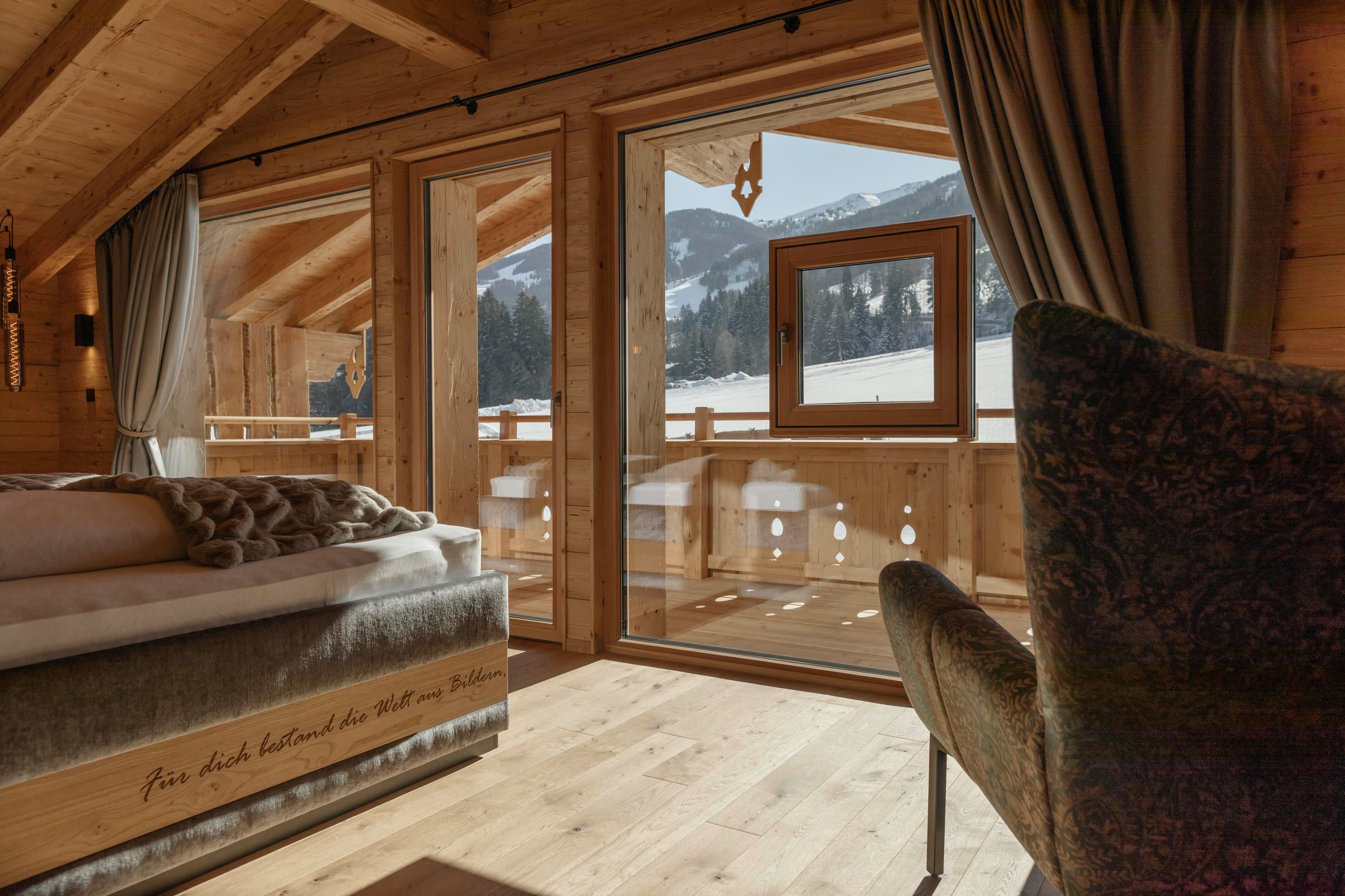 Eine gemütliche Holzwohnung mit großen Fenstern und Blick auf schneebedeckte Berge. Die Einrichtung ist modern und einladend, ideal für einen entspannten Aufenthalt.