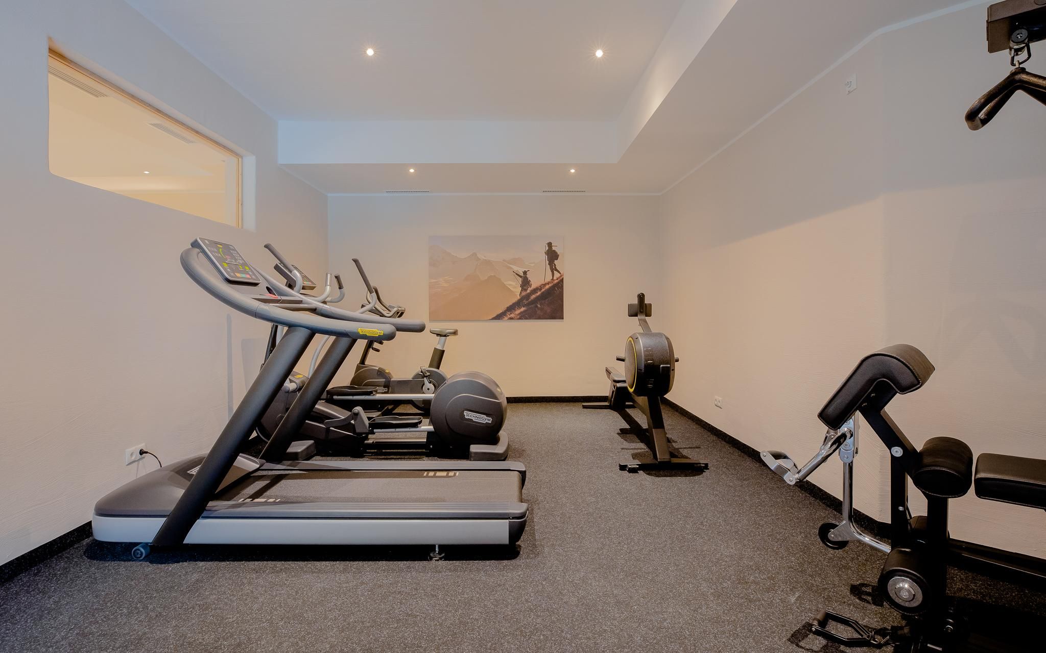Ein modernes Fitnessstudio mit Laufbändern und einem Rudergerät. Die Wände sind hell gestrichen und es gibt eine motivierende Wandkunst.