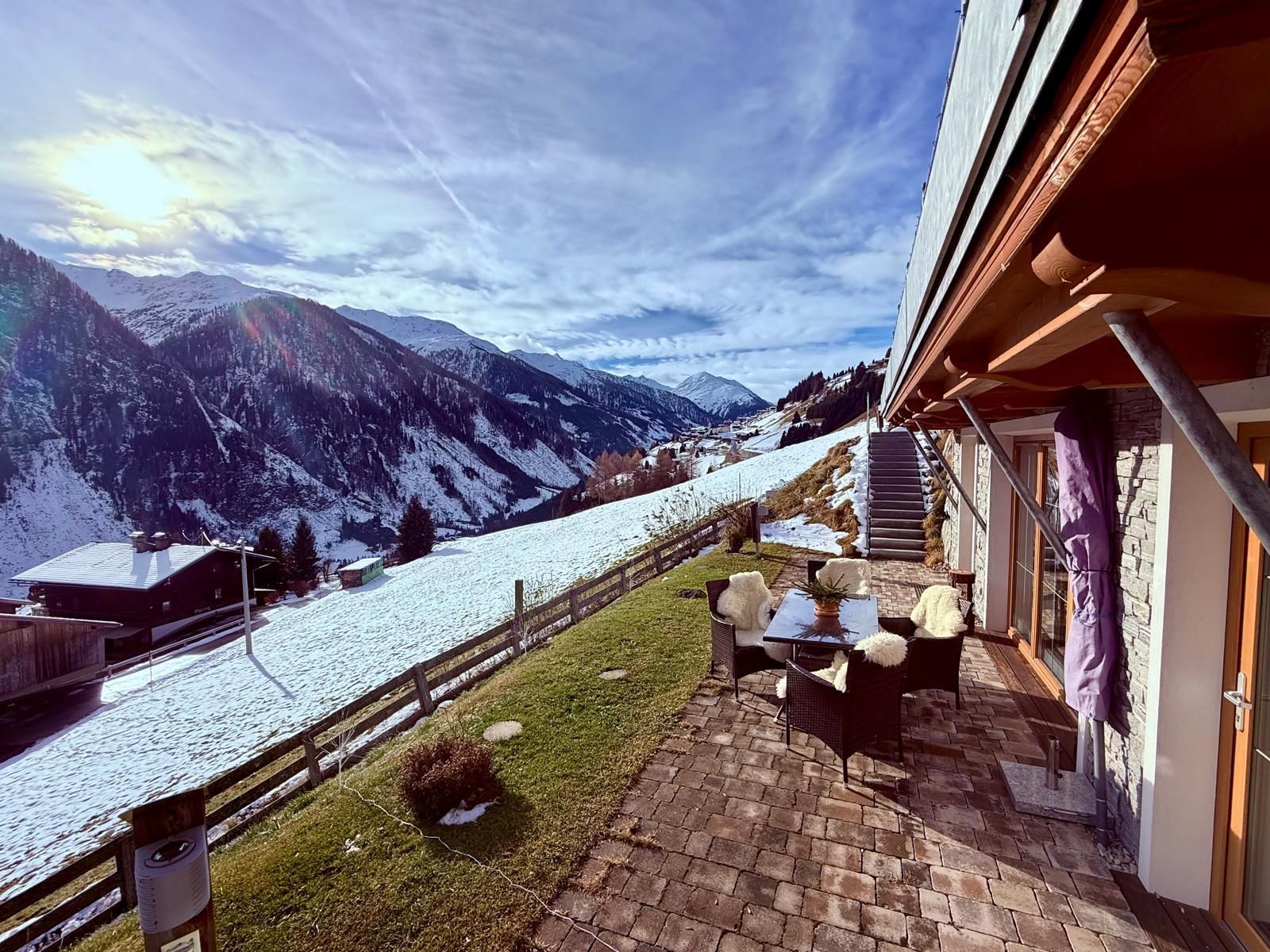 Eine wunderschöne Berglandschaft mit schneebedeckten Hängen und einem klaren Himmel. Auf der terrasse steht ein Sitzbereich mit Blick auf die Berge.