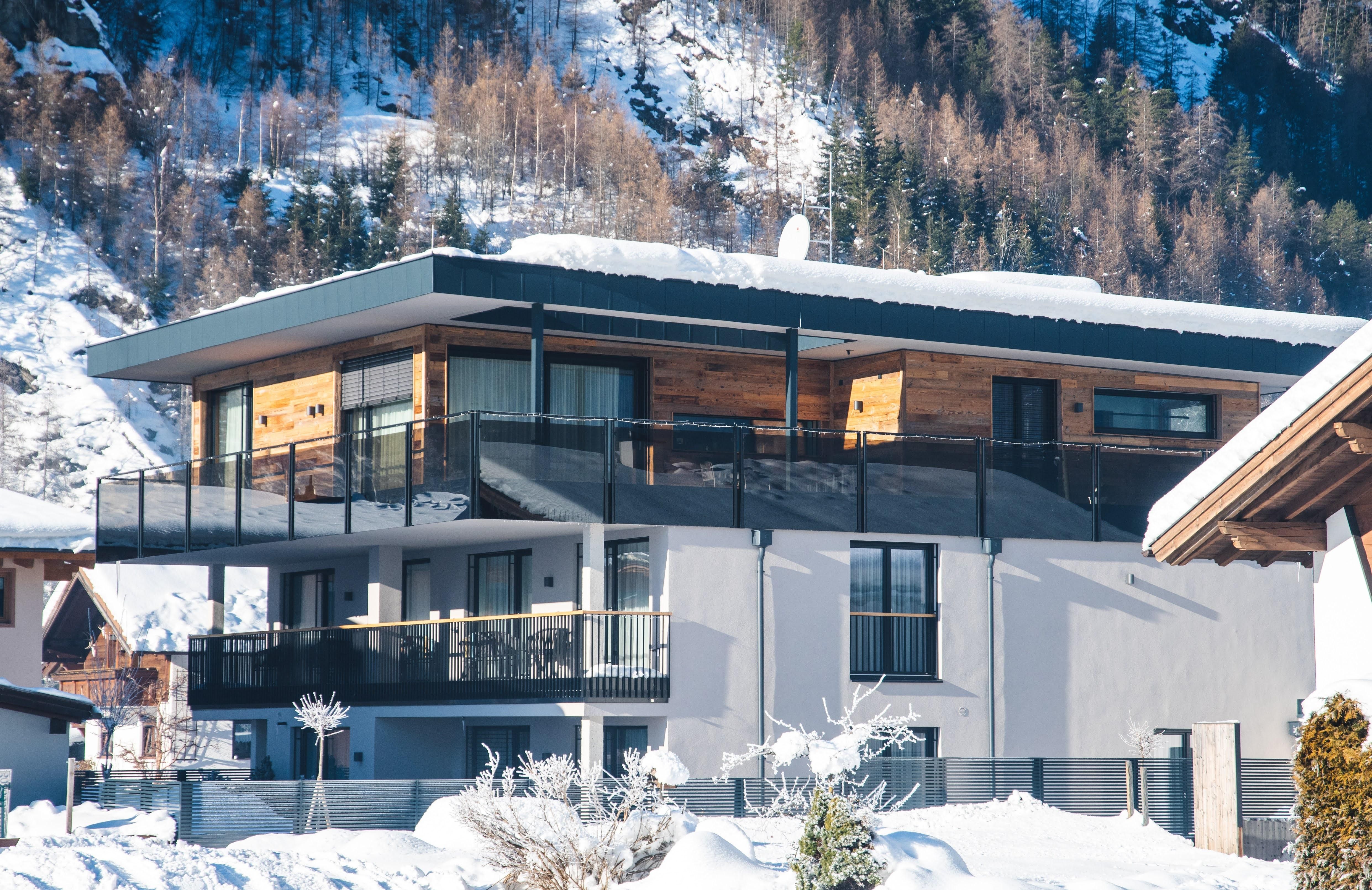 Ein modernes Gebäude im Schnee, umgeben von Bergen. Die Architektur kombiniert Holz und Glas und bietet einen gemütlichen Eindruck.