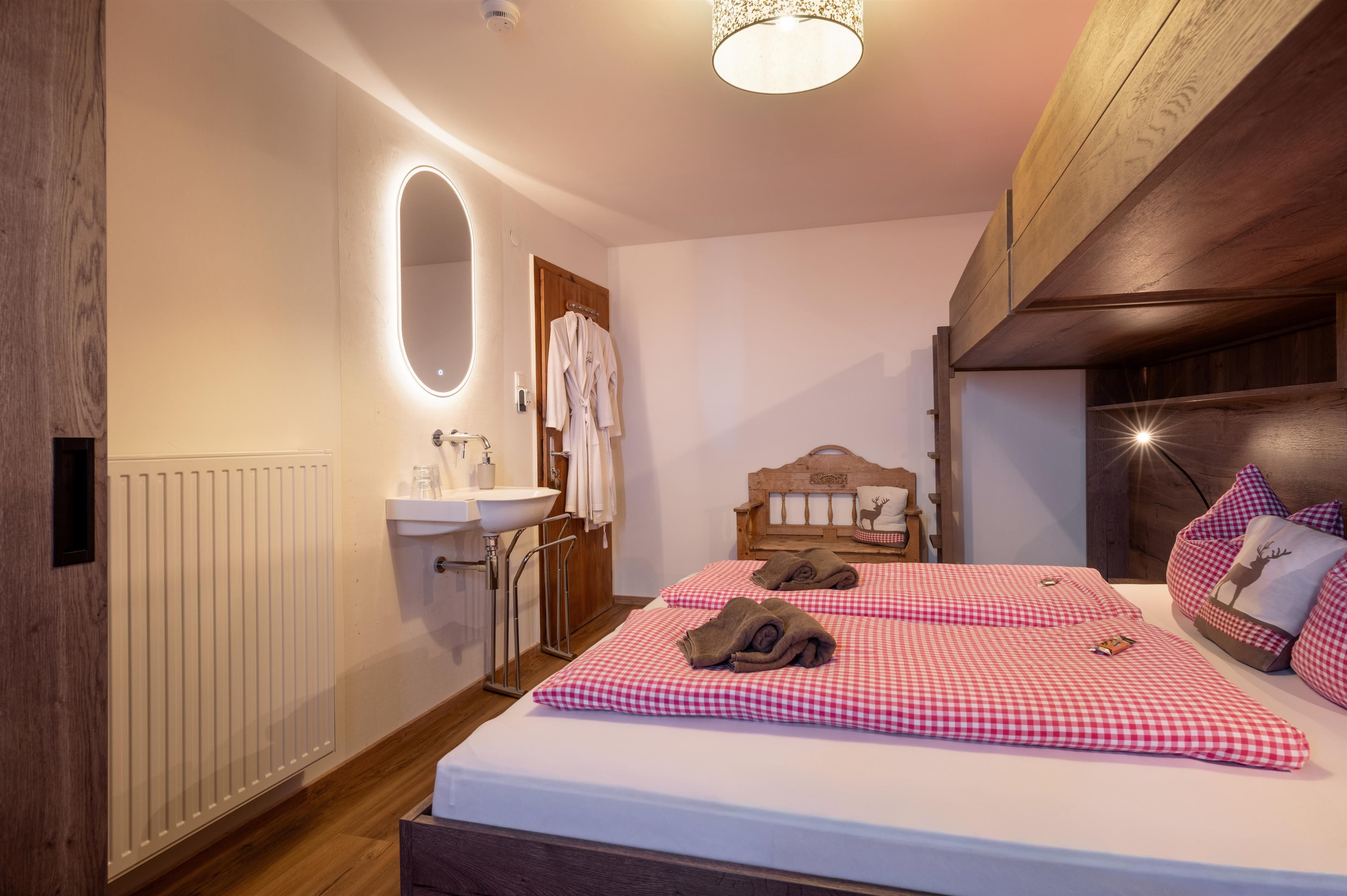 Ein modernes Schlafzimmer mit einem Doppelbett und karierten Kissen. Der Raum ist hell und freundlich eingerichtet, mit einem Waschbecken und einem Spiegel an der Wand.