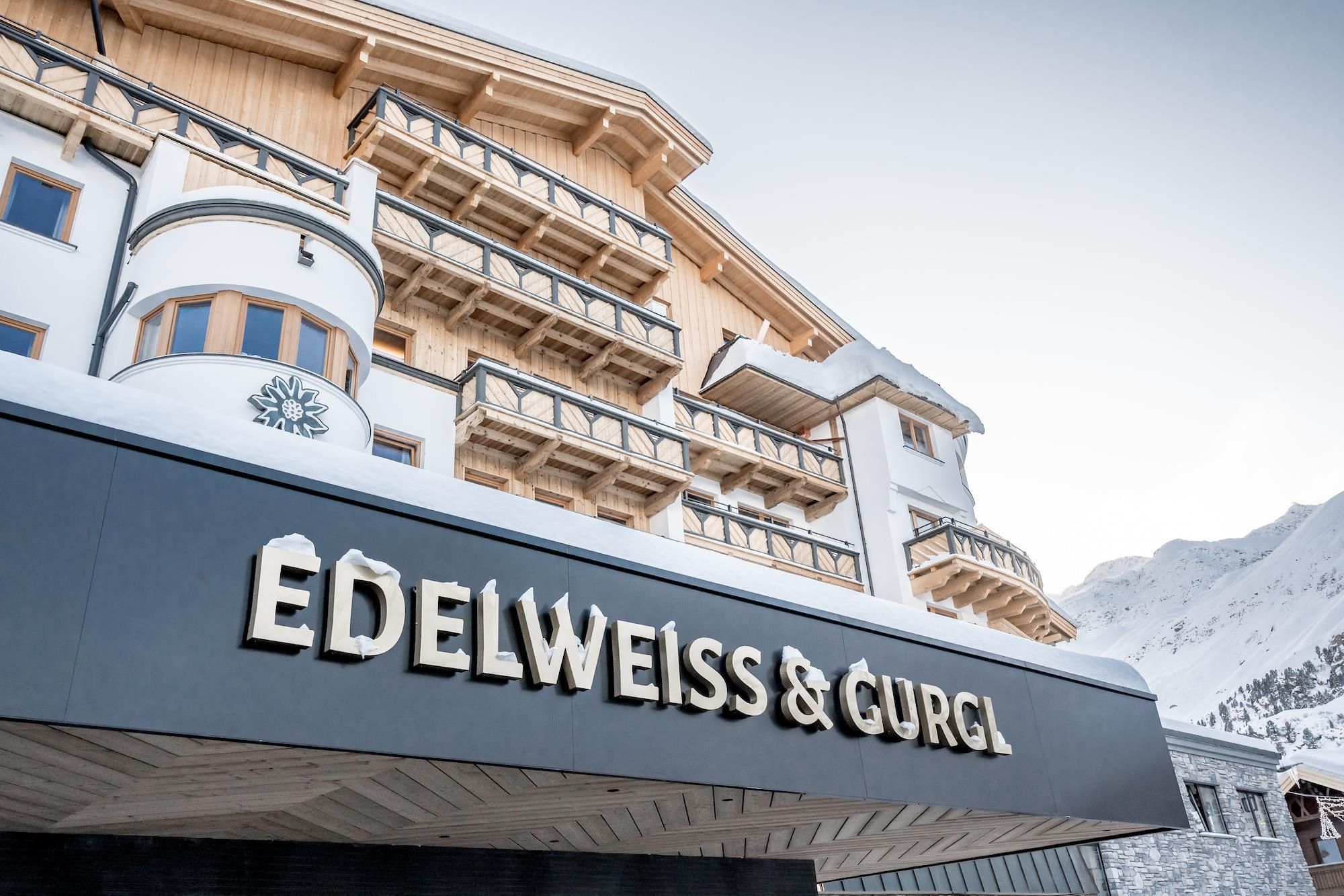 Ein modernes Hotelgebäude im alpinen Stil, umgeben von Schnee. Über dem Eingang steht der Name „EDELWEISS & GURGL“.