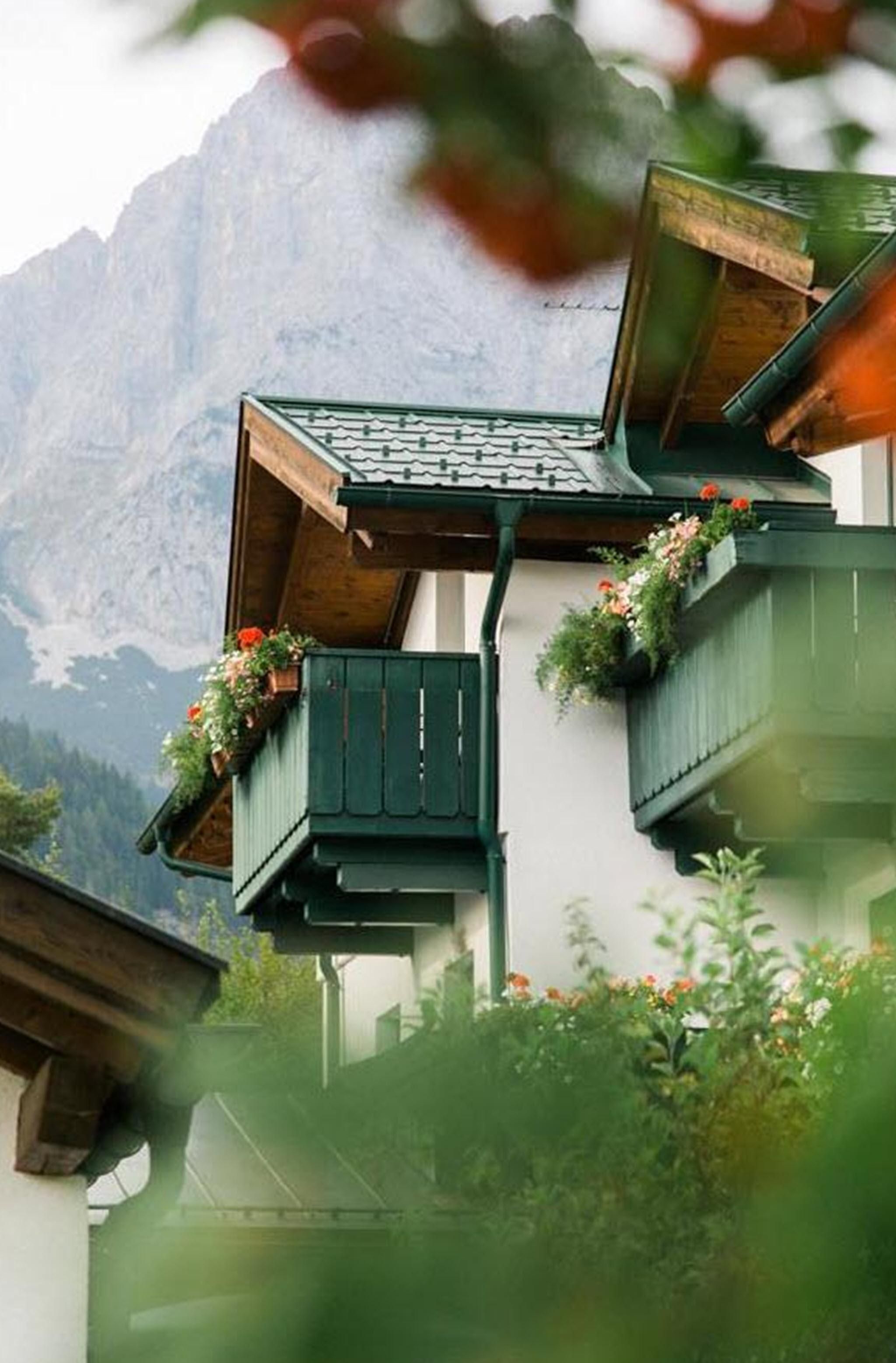 Ein wunderschönes Haus mit einem Balkon, geschmückt mit Blumen. Im Hintergrund sind die Berge sichtbar.
