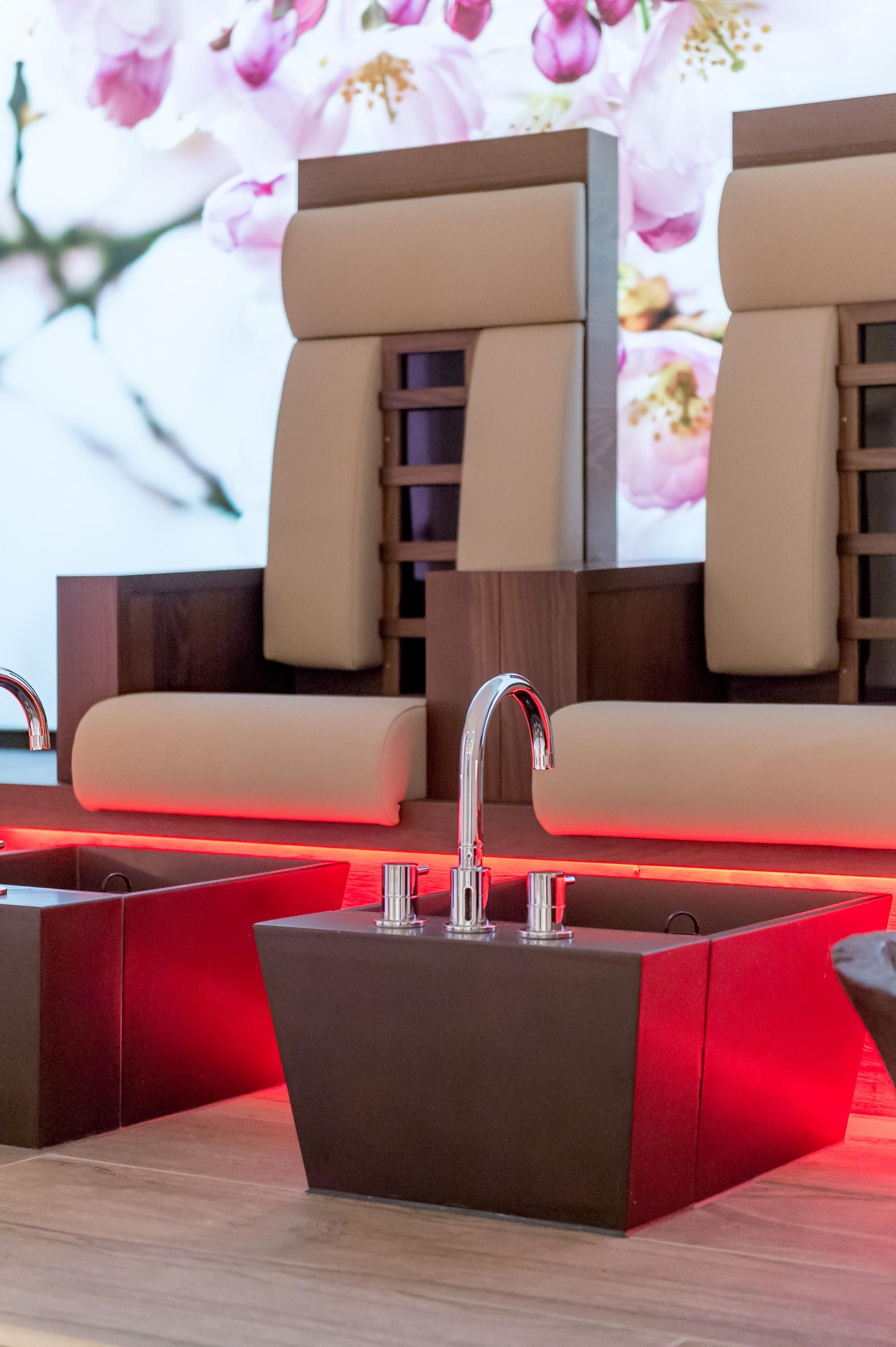 Zwei bequeme Stühle mit modischem Design stehen vor einer Wand mit blühenden Blumen. Daneben befinden sich moderne Fußbadewannen mit LED-Beleuchtung.