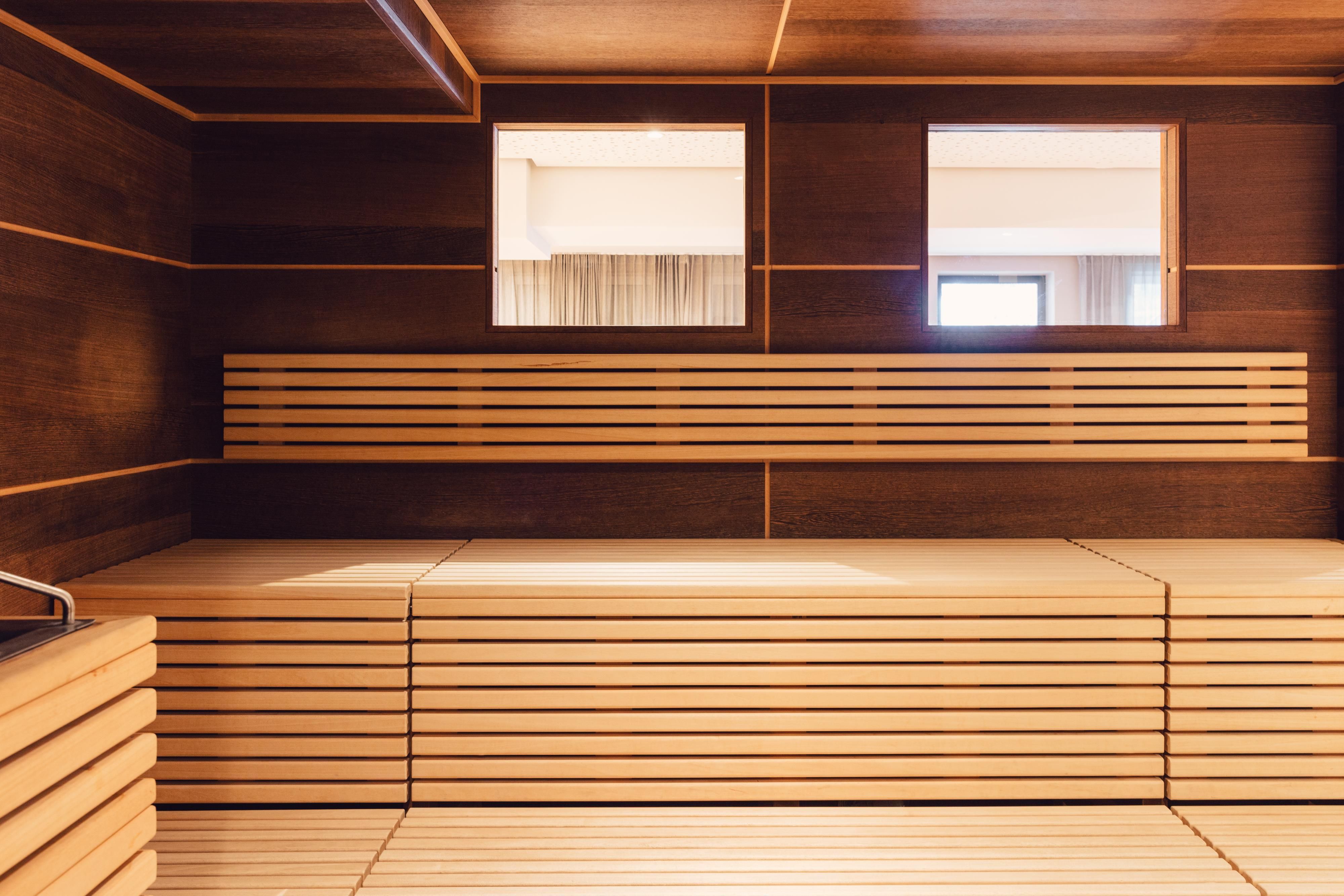Ein gemütlicher Sauna-Raum mit Holzbänken und Fenstern. Die warme Holzoptik schafft eine entspannende Atmosphäre.