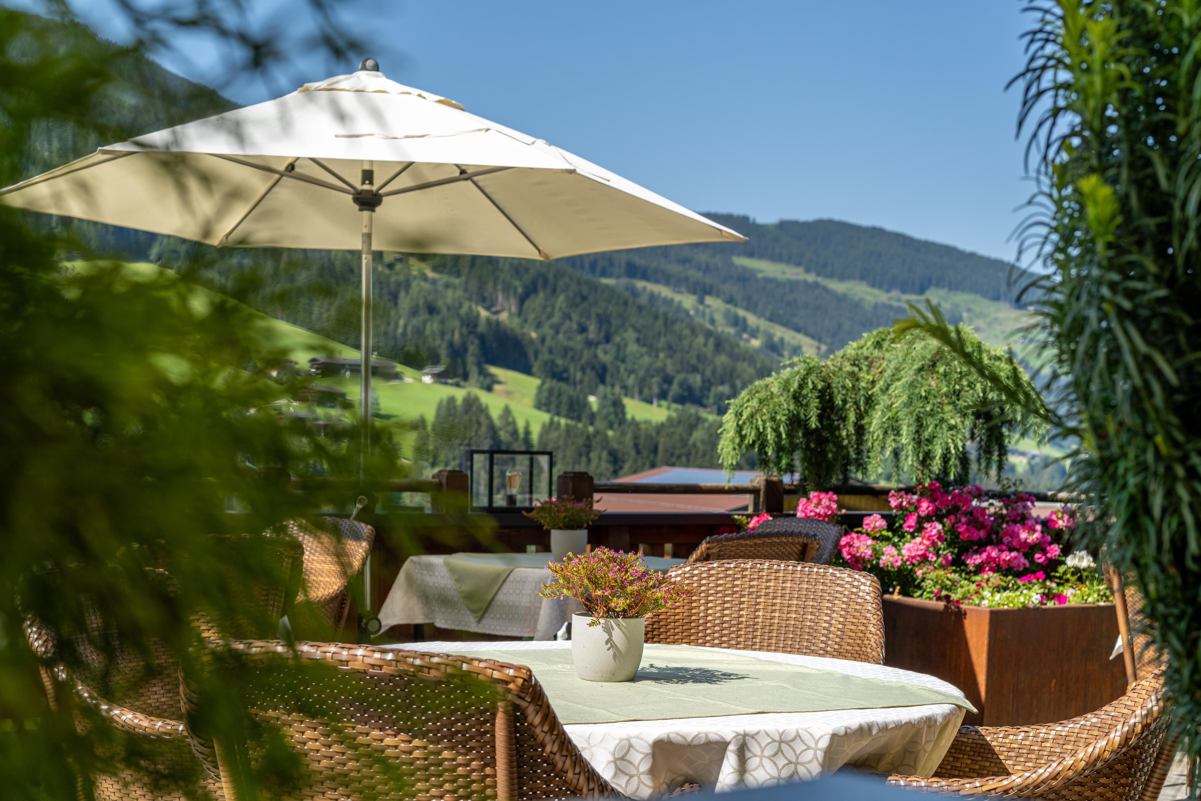 Ein schöner Außenbereich mit Rattanmöbeln und Sonnenschirm. Blumen und grüne Landschaften sorgen für eine einladende Atmosphäre.