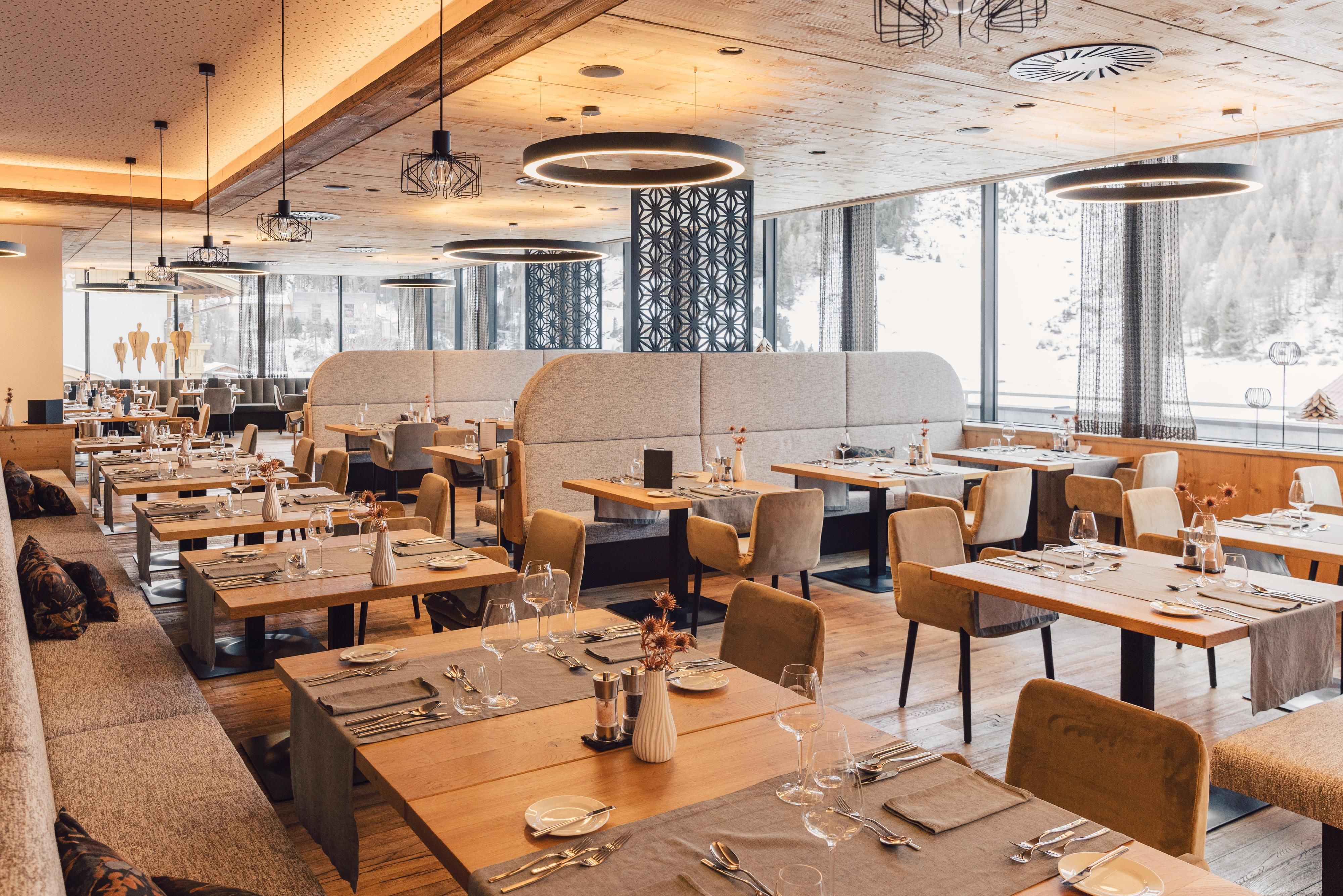 Ein modernes Restaurant mit eleganten Tischen und Stühlen. Große Fenster bieten einen Blick auf die Natur.