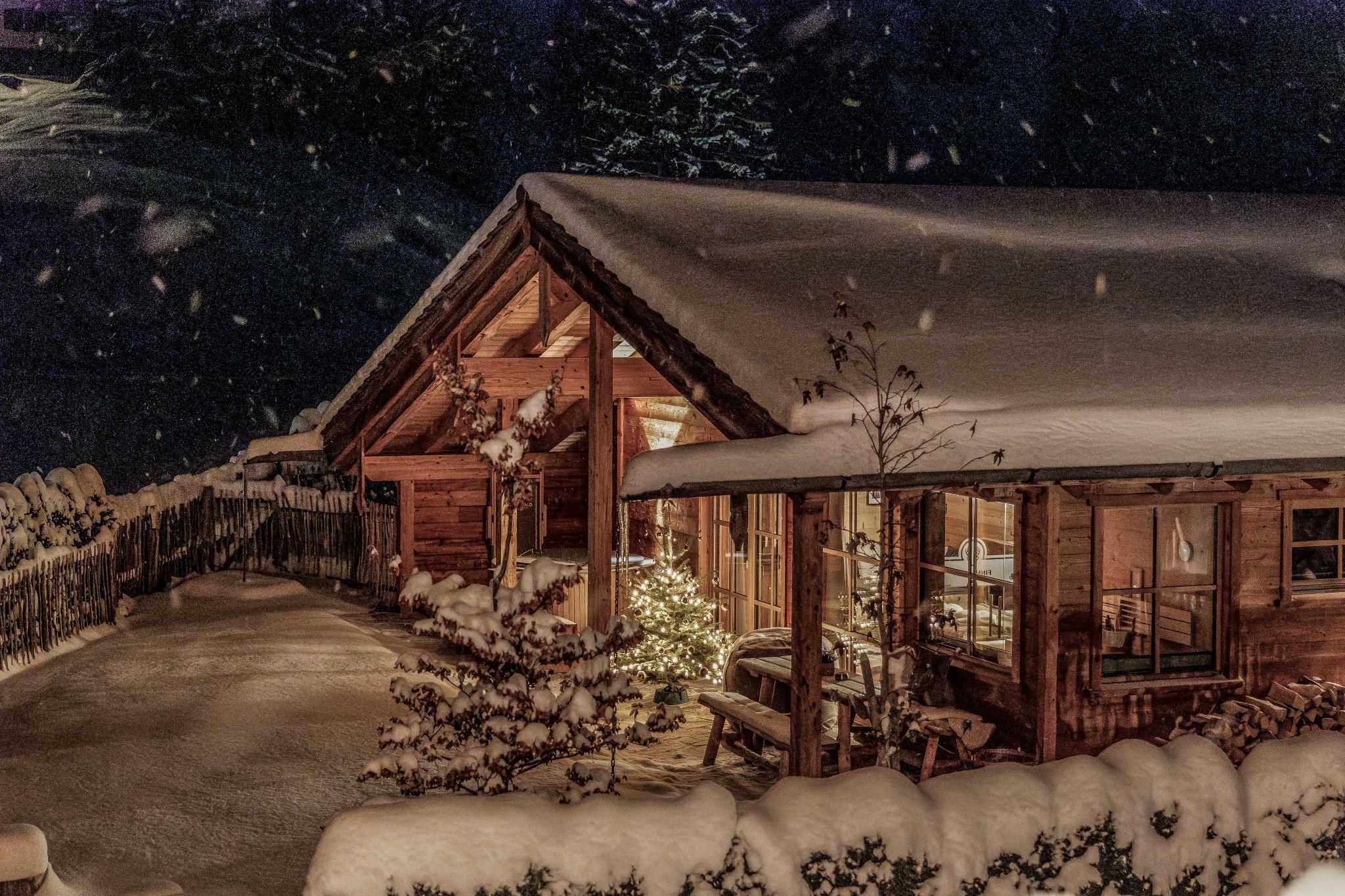 Ein hübsches Chalet, das unter einer Schneeschicht versteckt ist. Die Umgebung ist winterlich und festlich beleuchtet.